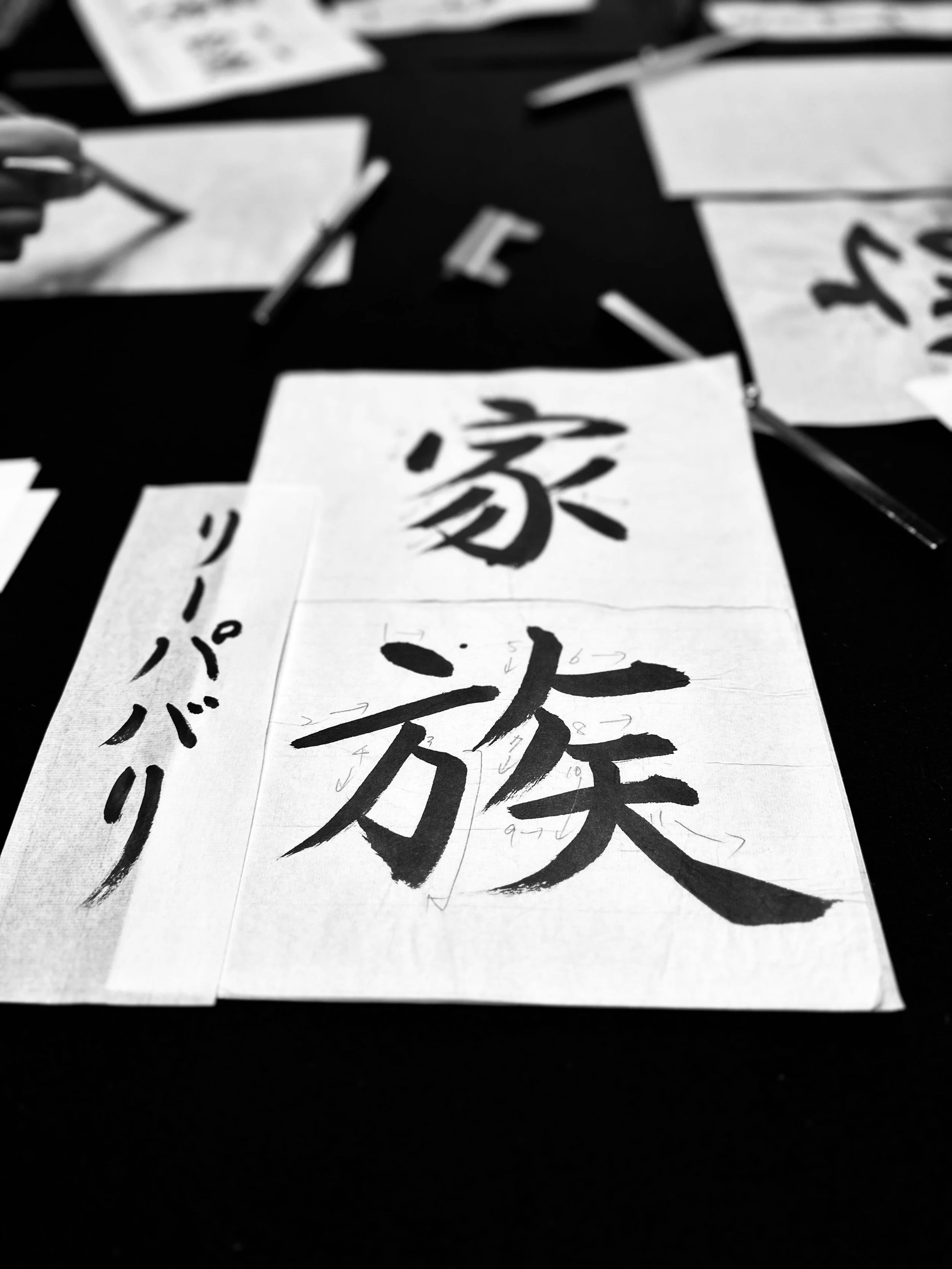 Sheets of paper with Japanese calligraphy characters scattered on a dark surface.