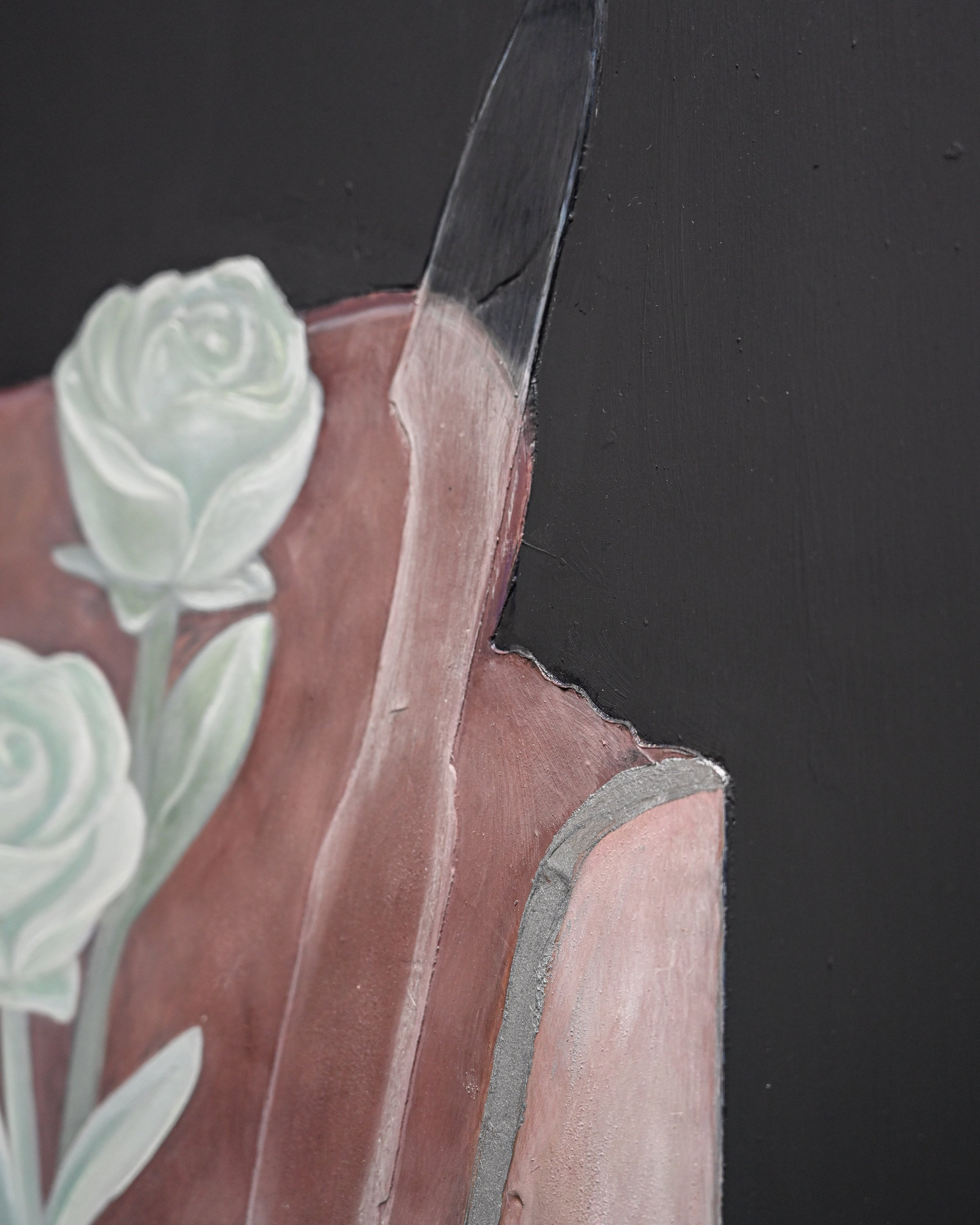 Close-up view of a ceramic or porcelain decorative item with a rose design, partially visible on the left side. The item seems to be leaning against a black surface with multiple horizontal layers or sections of varying colors and textures.