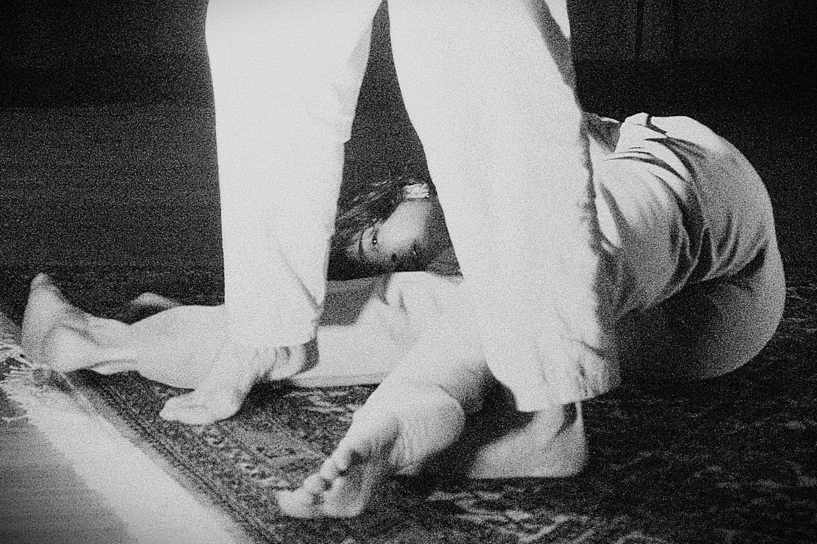 A person wearing a hooded sweatshirt and glasses, kneeling on the floor, appears to be cleaning or wiping a small dog with a towel on a patterned rug.
