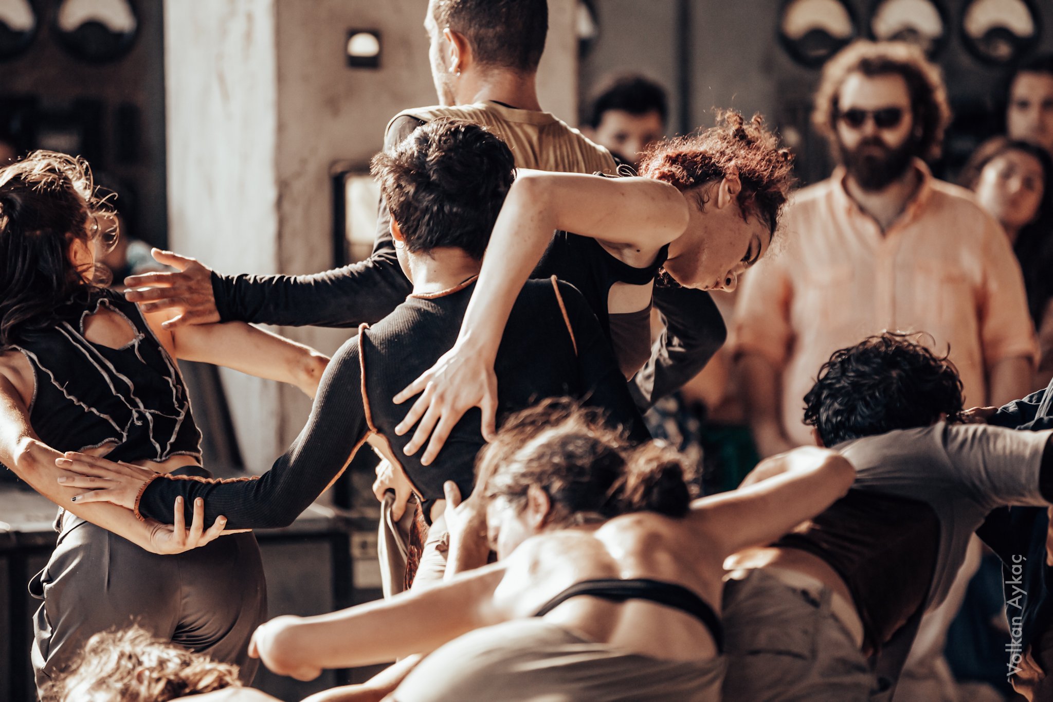 A group of people appear to be dancing or engaging in a lively activity, with some individuals embracing or reaching out to each other in a crowded indoor setting.