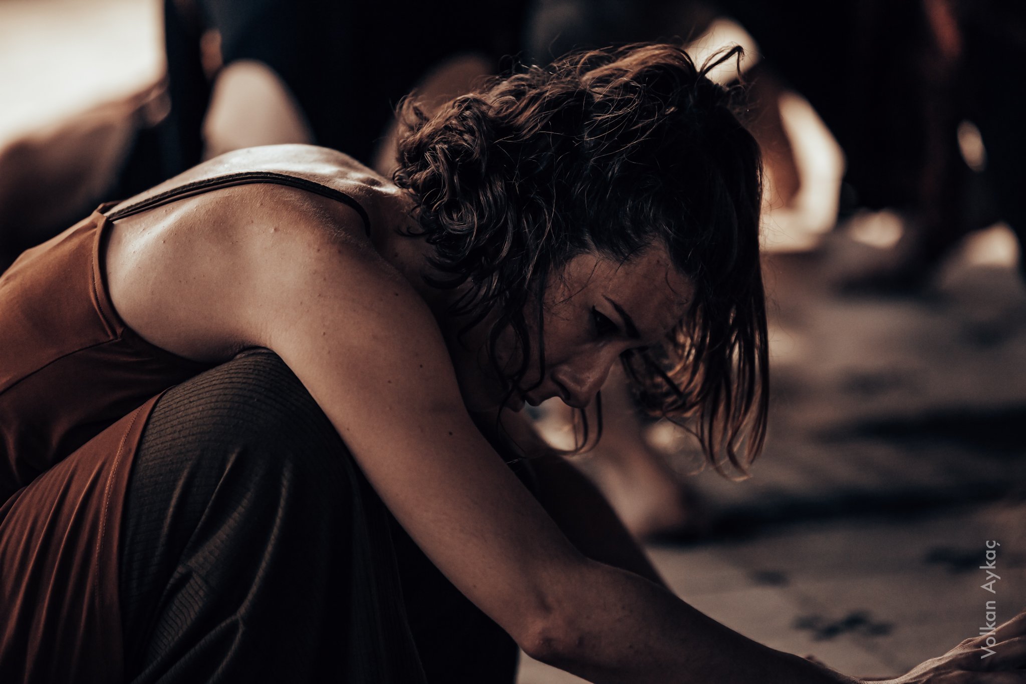 A woman with curly hair and glasses is sitting on the floor, leaning forward with her head down and an expression of distress.