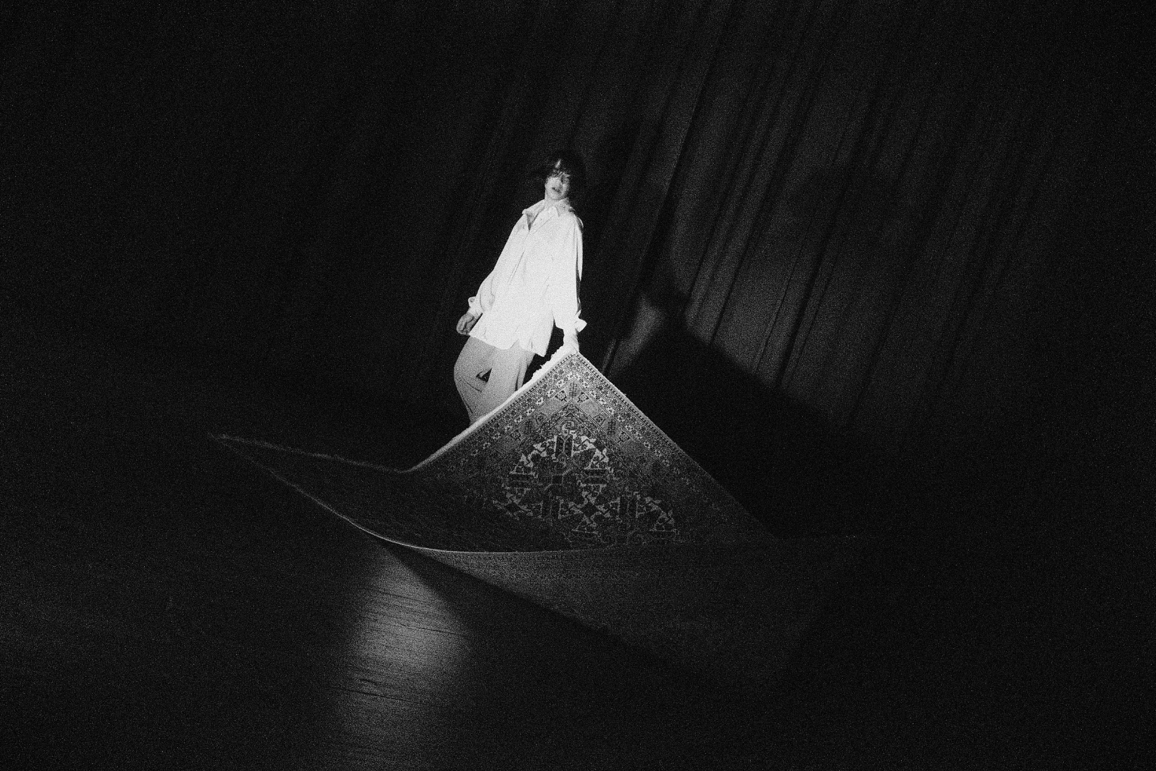 A person standing on the edge of a rolled-out rug in a dark room.