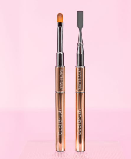 Pennelli per unghie con manici dorati e punte diverse, uno a forma di spazzola e l'altro a spatola, su sfondo rosa.