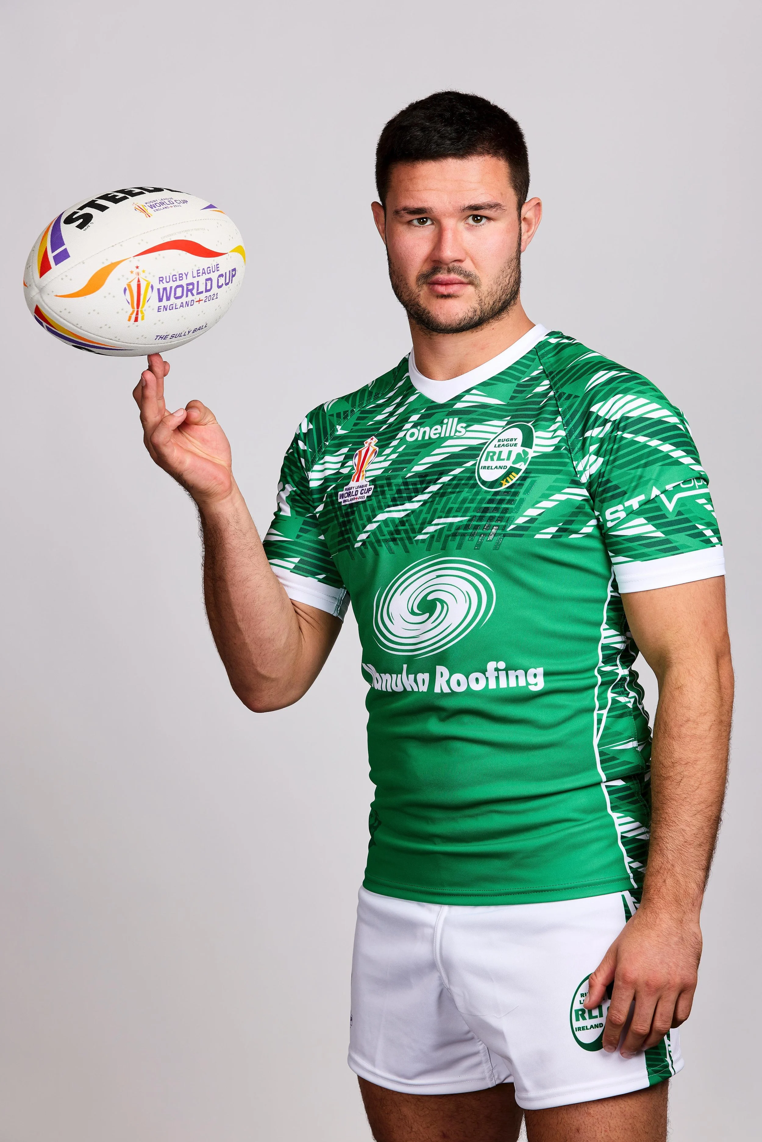 A rugby player wearing a green and white team jersey holding a rugby ball with the World Cup logo, standing against a plain background.