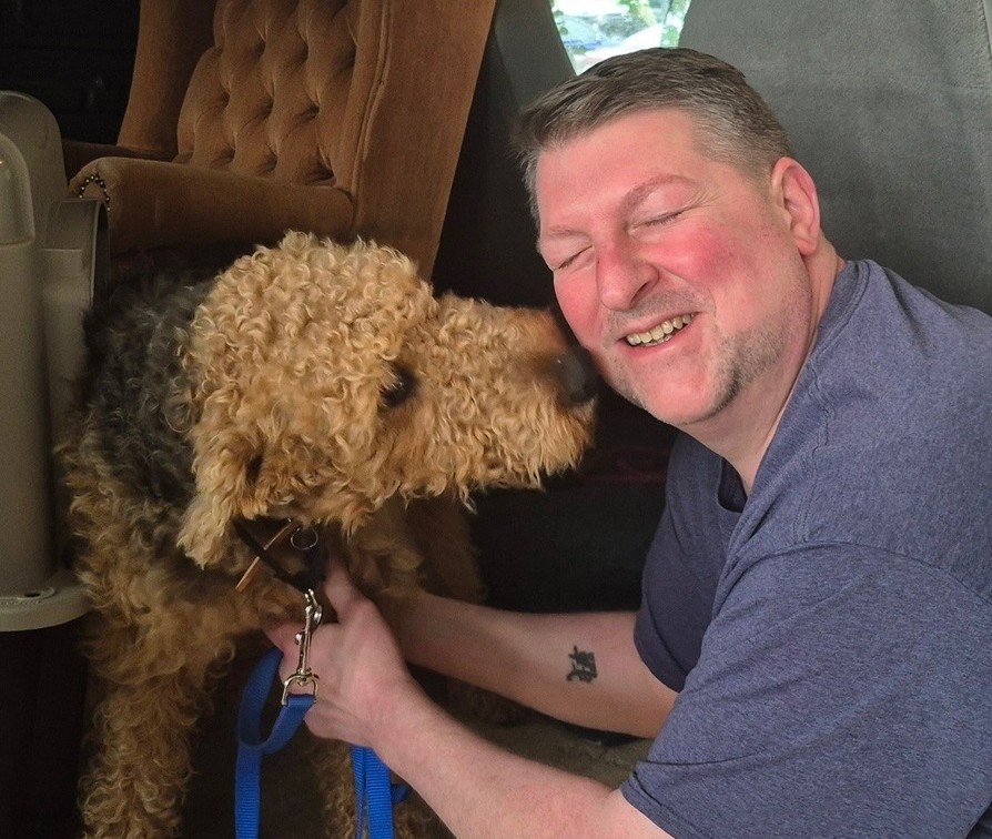 A man smiling with closed eyes while holding a curly-haired dog close to his face.