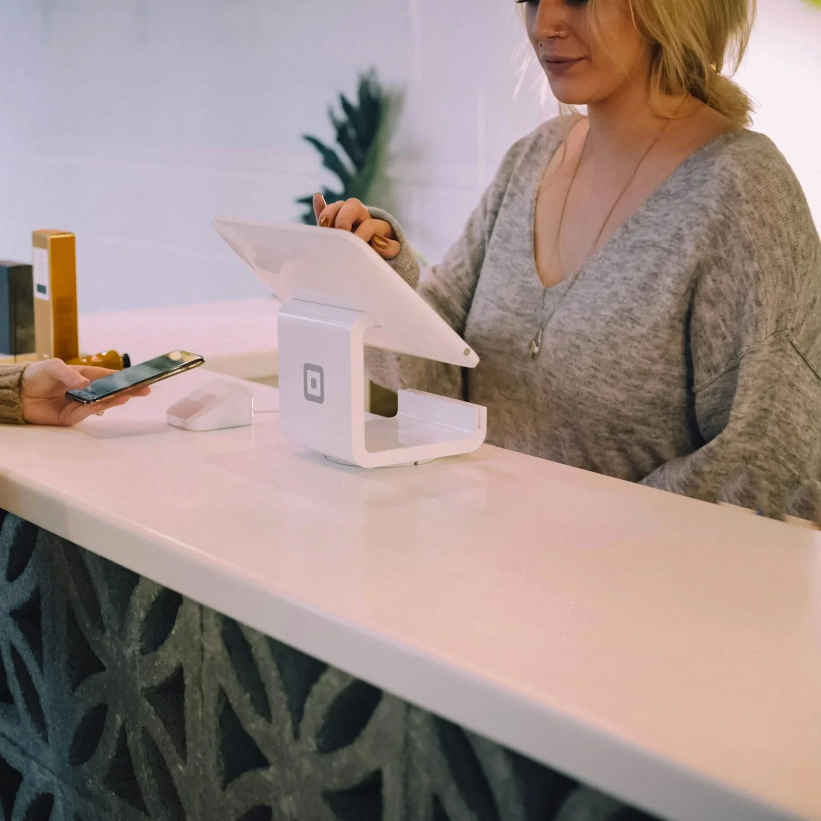 A customer at a counter making a payment using a smartphone while a cashier operates a point-of-sale system in a modern, well-lit space.