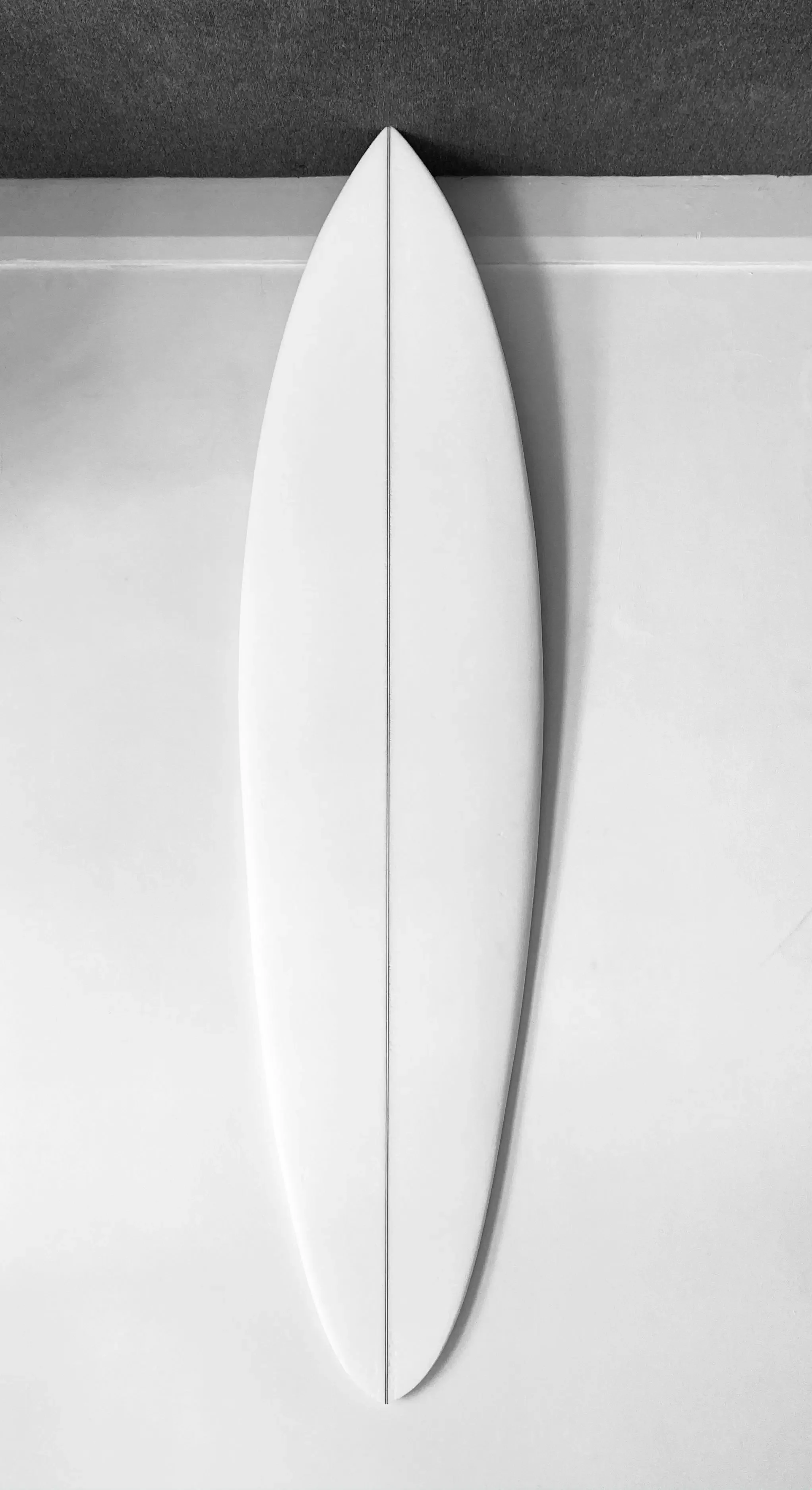 A white surfboard with a black line down the center, resting against a white wall.