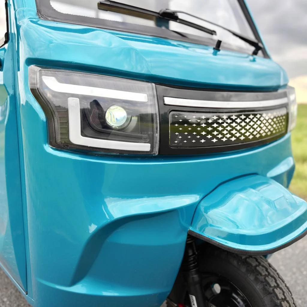 Nærbillede af fronten af en luxcap el-kabinescooter, herunder frontlygter, forhjul, og passagerkasse med vindue.