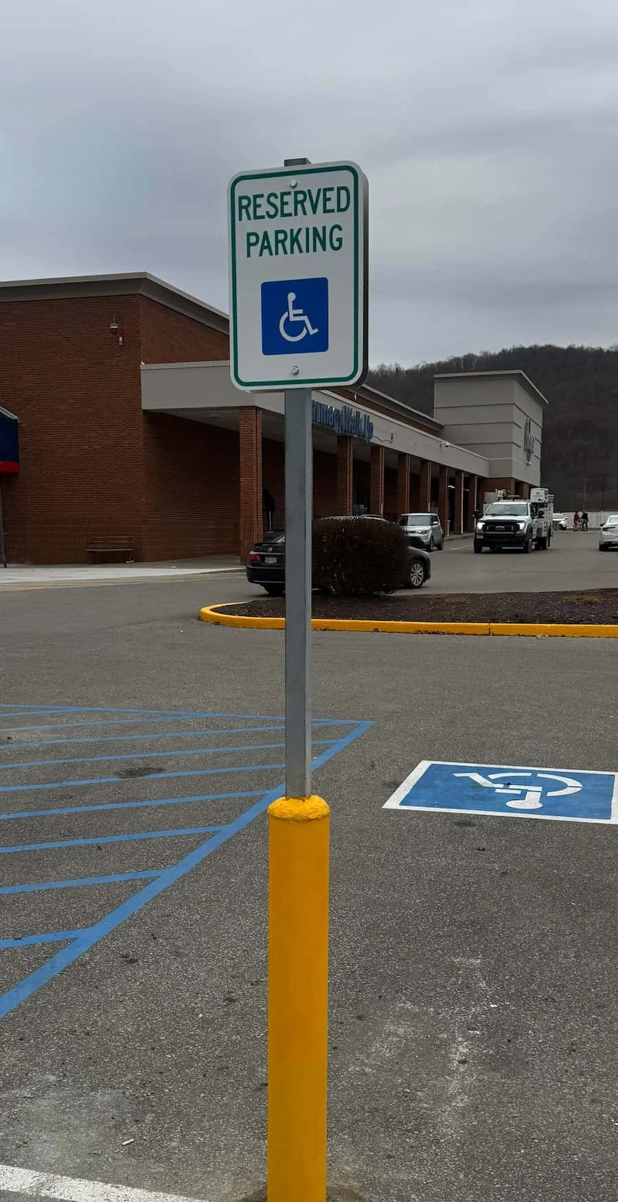 A parking lot with an accessible parking sign and a reserved parking space for people with disabilities, outside a shopping center.