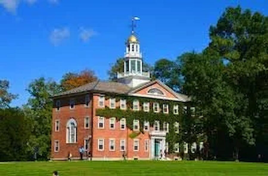 A red brick historic building with white accents, a tall clock tower with a gold dome, surrounded by green trees, under a blue sky.