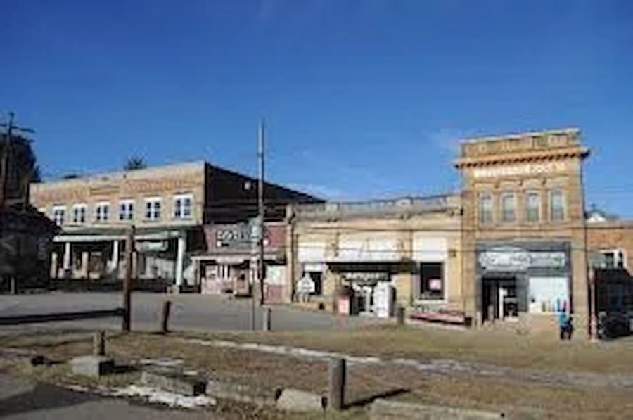 A small town street with old brick buildings, some with storefronts, under a clear blue sky.