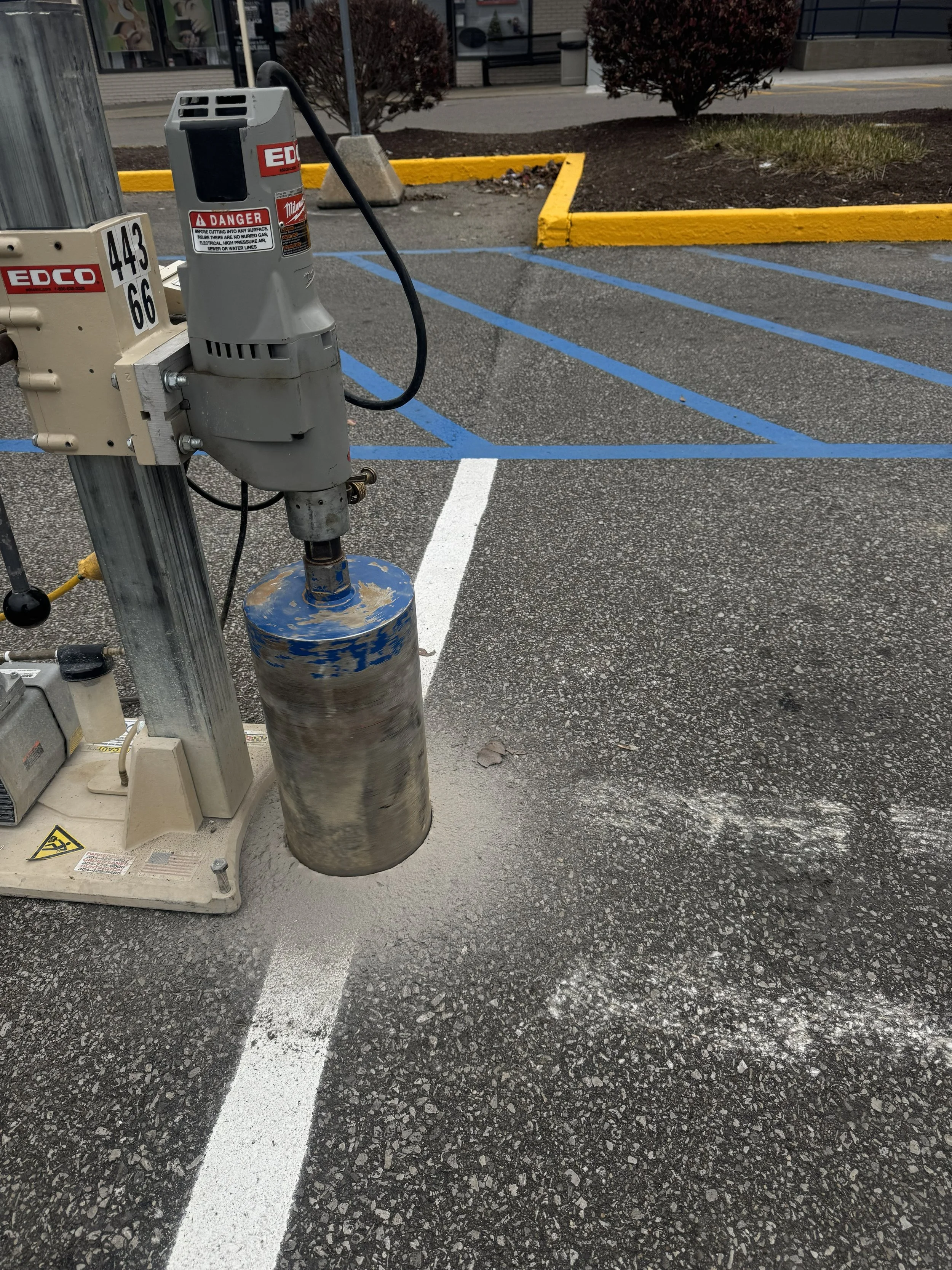 Parking lot with a blue-striped wheelchair accessible parking space, a yellow curb, and a traffic cone in the background.