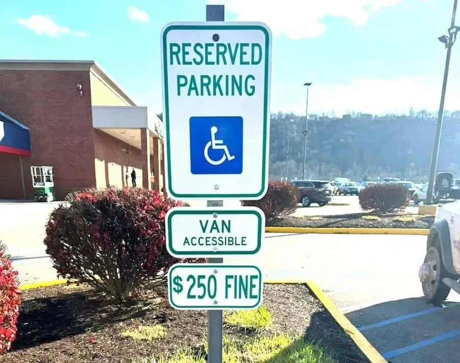 Parking sign indicating reserved parking for handicapped and van accessible, with a $250 fine for violations, located in a shopping plaza parking lot.