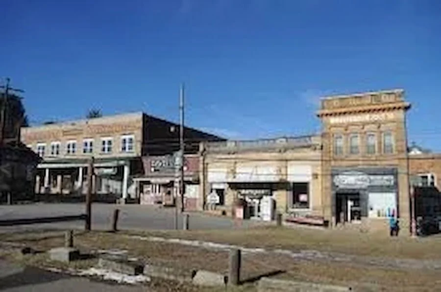 A small downtown street with older brick buildings, some with storefronts, under a clear blue sky.