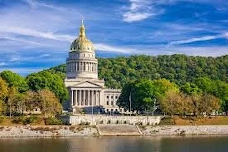 The Arkansas State Capitol building with a gold dome, surrounded by trees and hills, located along a river in Little Rock, Arkansas.