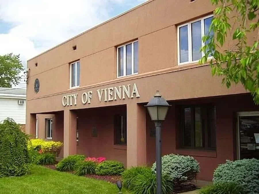 Front view of a building labeled 'City of Vienna' with windows, a streetlamp, and landscaped bushes and flowers.