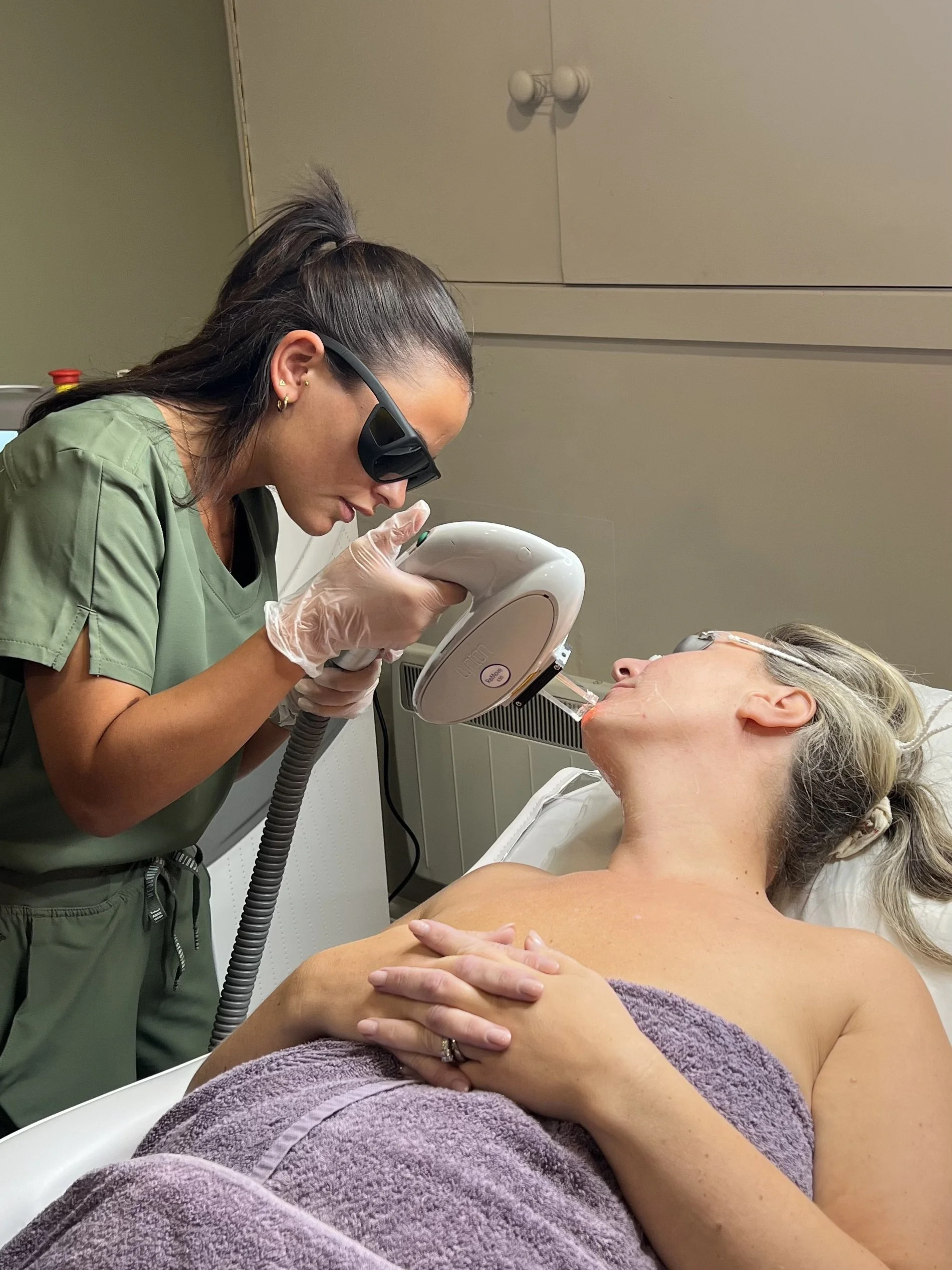 Medical professional performing a skin treatment on a woman lying in a hospital bed, using a handheld device and wearing protective goggles.