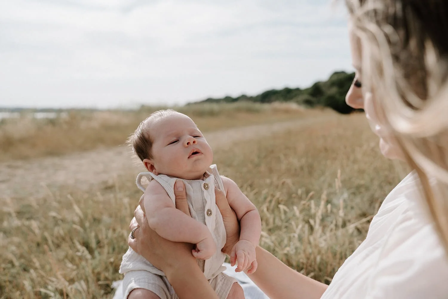 A woman holding a baby outside in a field with tall grass, both looking at each other.