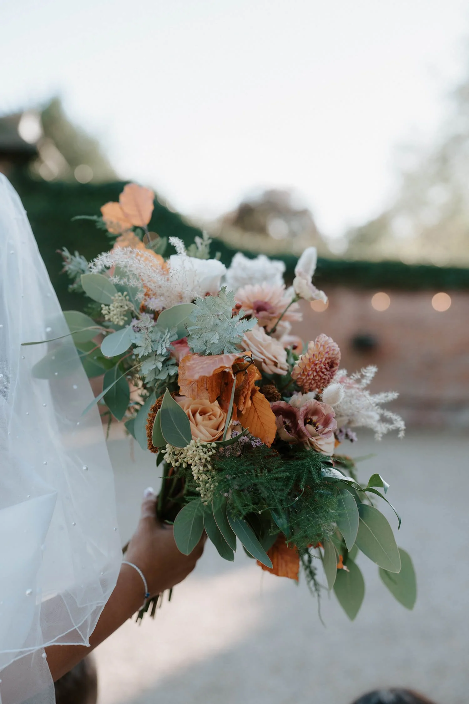 Person holding a bouquet of mixed flowers and greenery outdoors during daytime