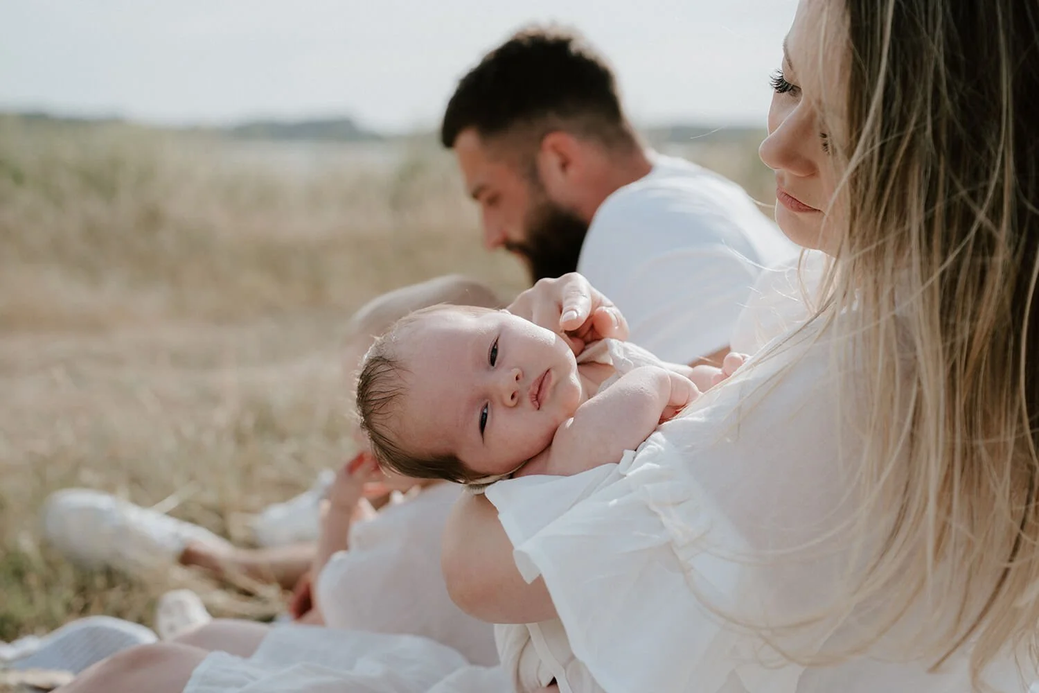 A woman holding a newborn baby outdoors with a man in the background.