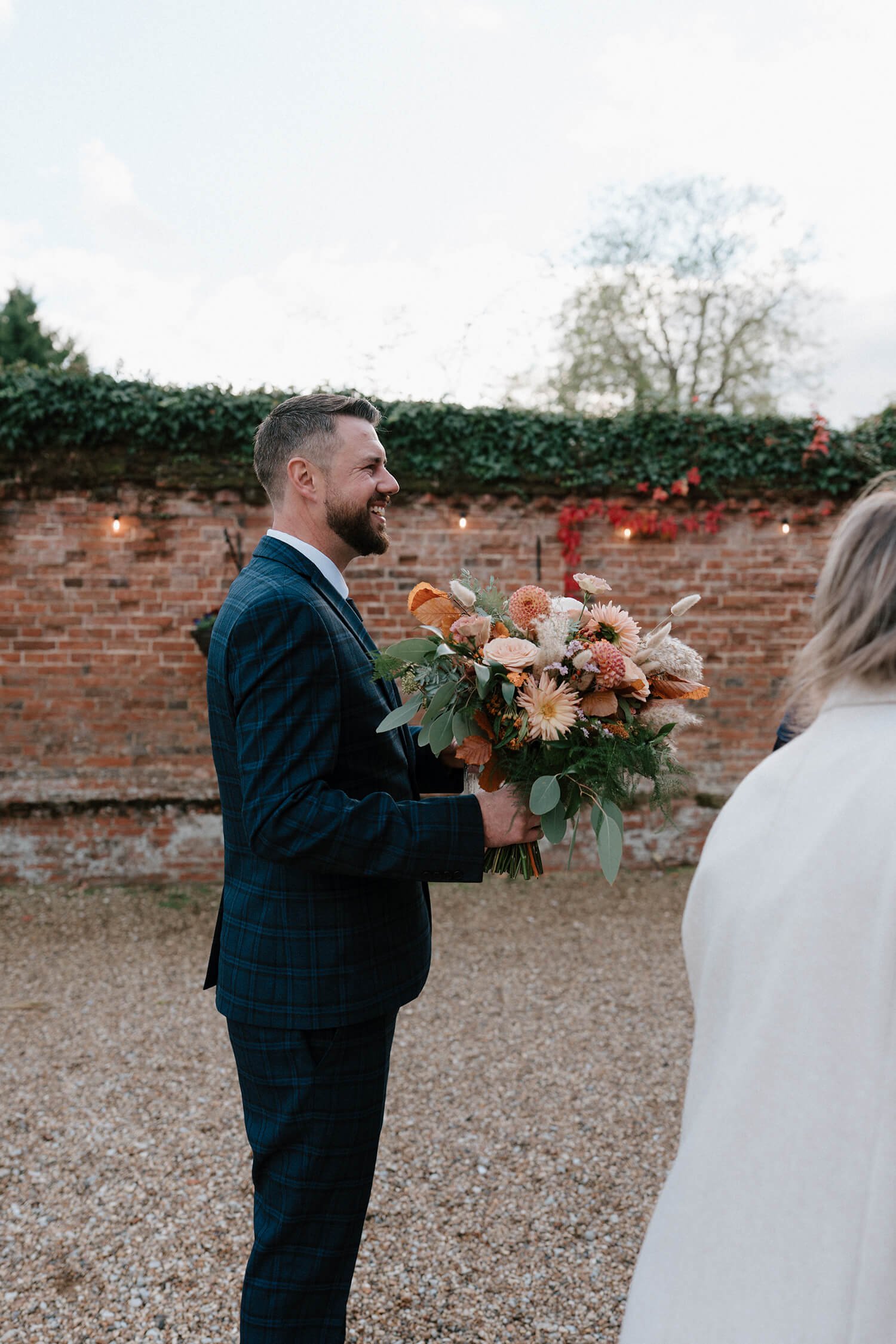 A man in a plaid suit holding a bouquet of flowers at an outdoor wedding or event.
