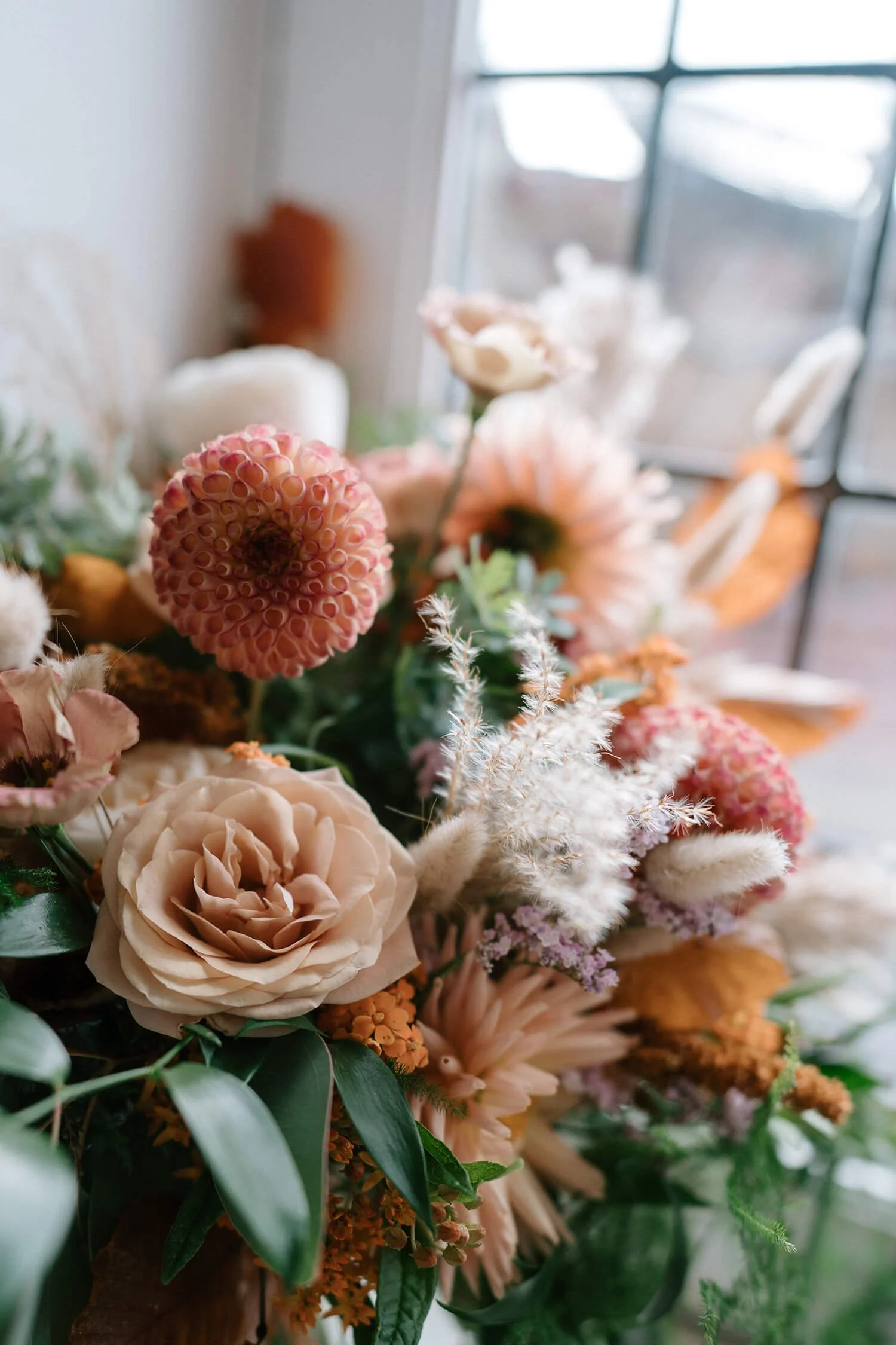 A bouquet of various pink, peach, and white flowers near a large window, with sunlight streaming in.