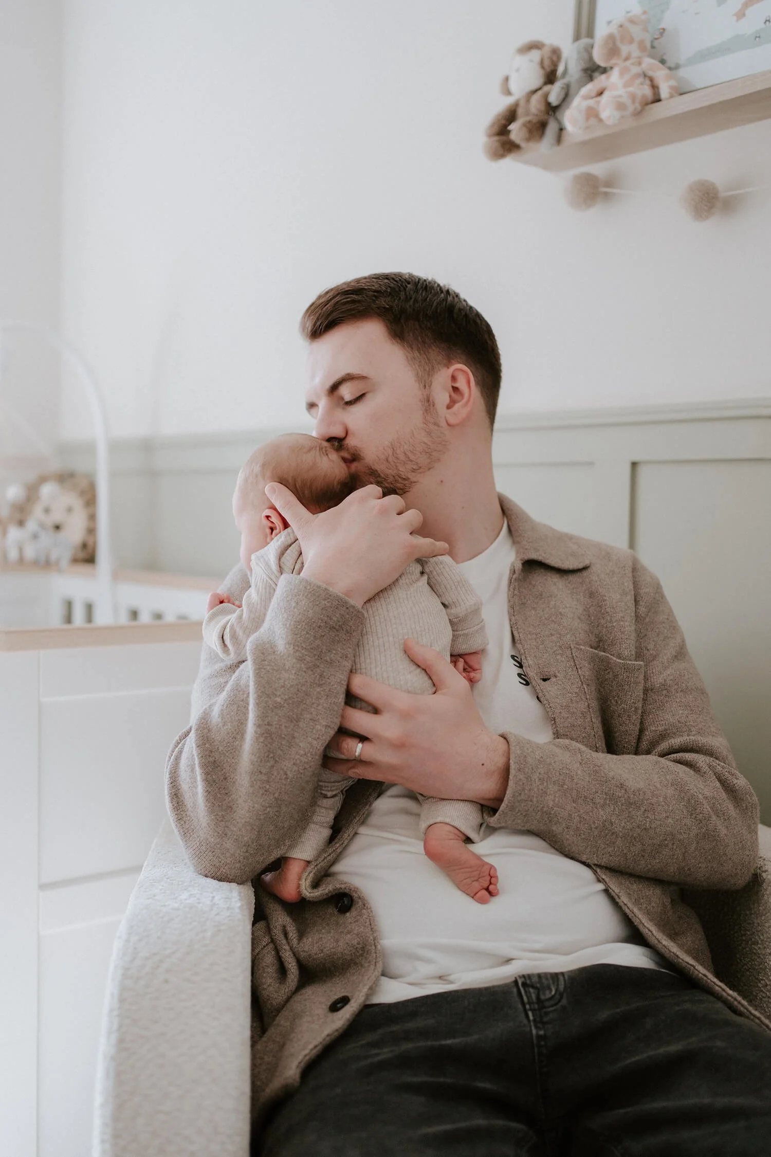 A man holding and kissing a newborn baby in a room decorated with plush toys and stuffed animals.