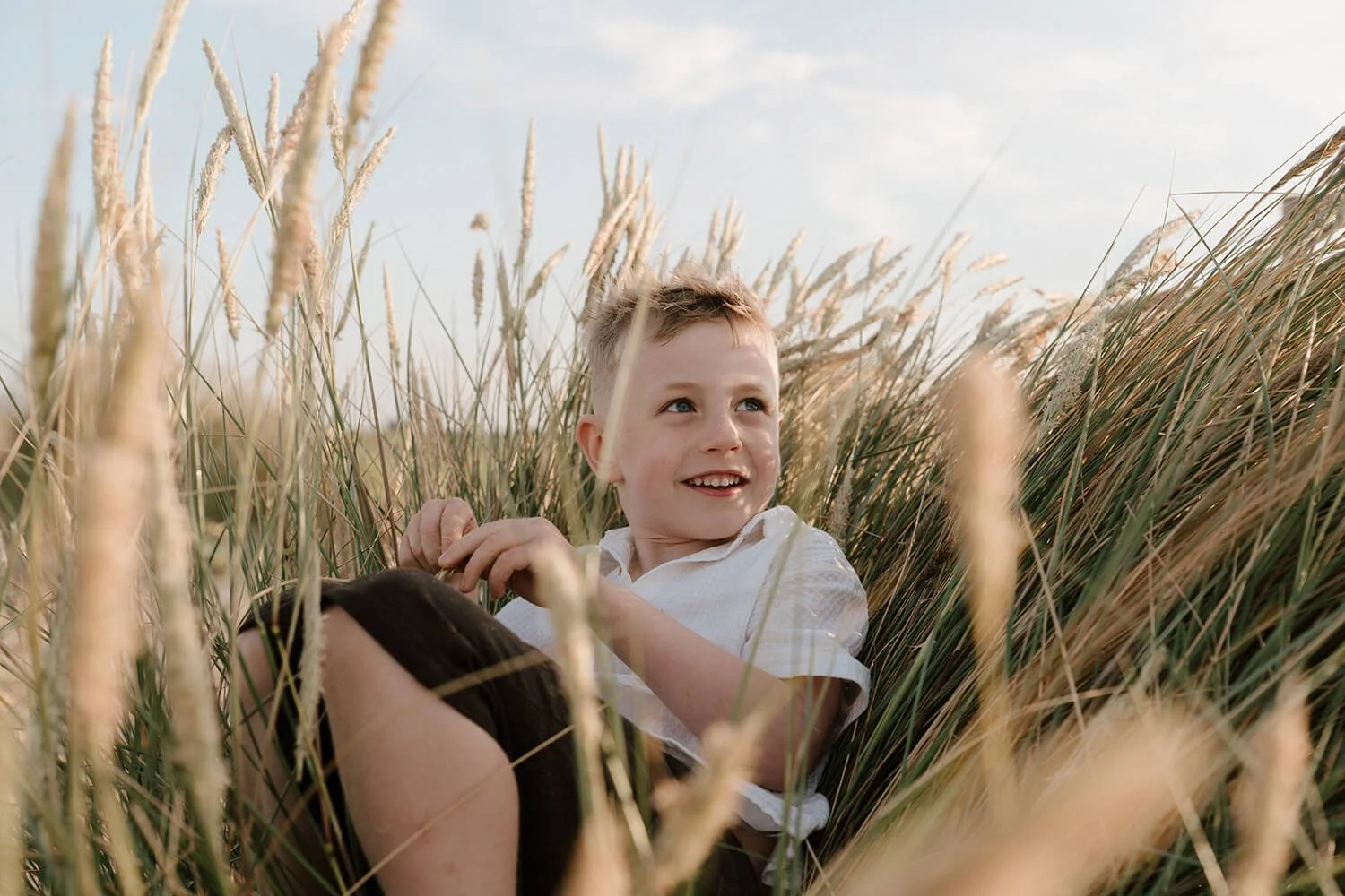 A young boy lying in a field of tall grass and looking up smiling