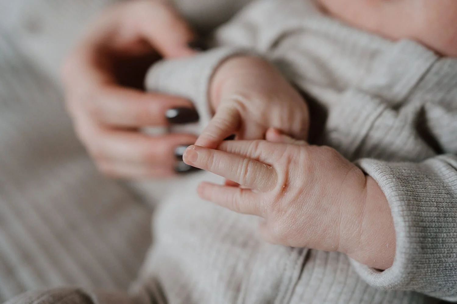 Close-up of an adult hand holding a baby's hand, with the baby's tiny fingers grasping the adult's finger.