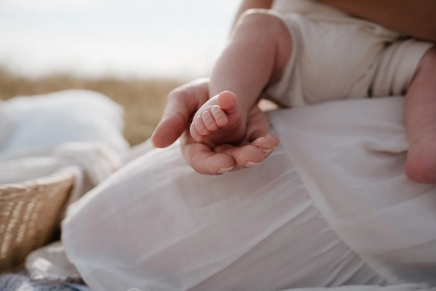 Close-up of a tiny baby's hand gripping an older person's finger, with soft natural lighting and a white blanket in the background.