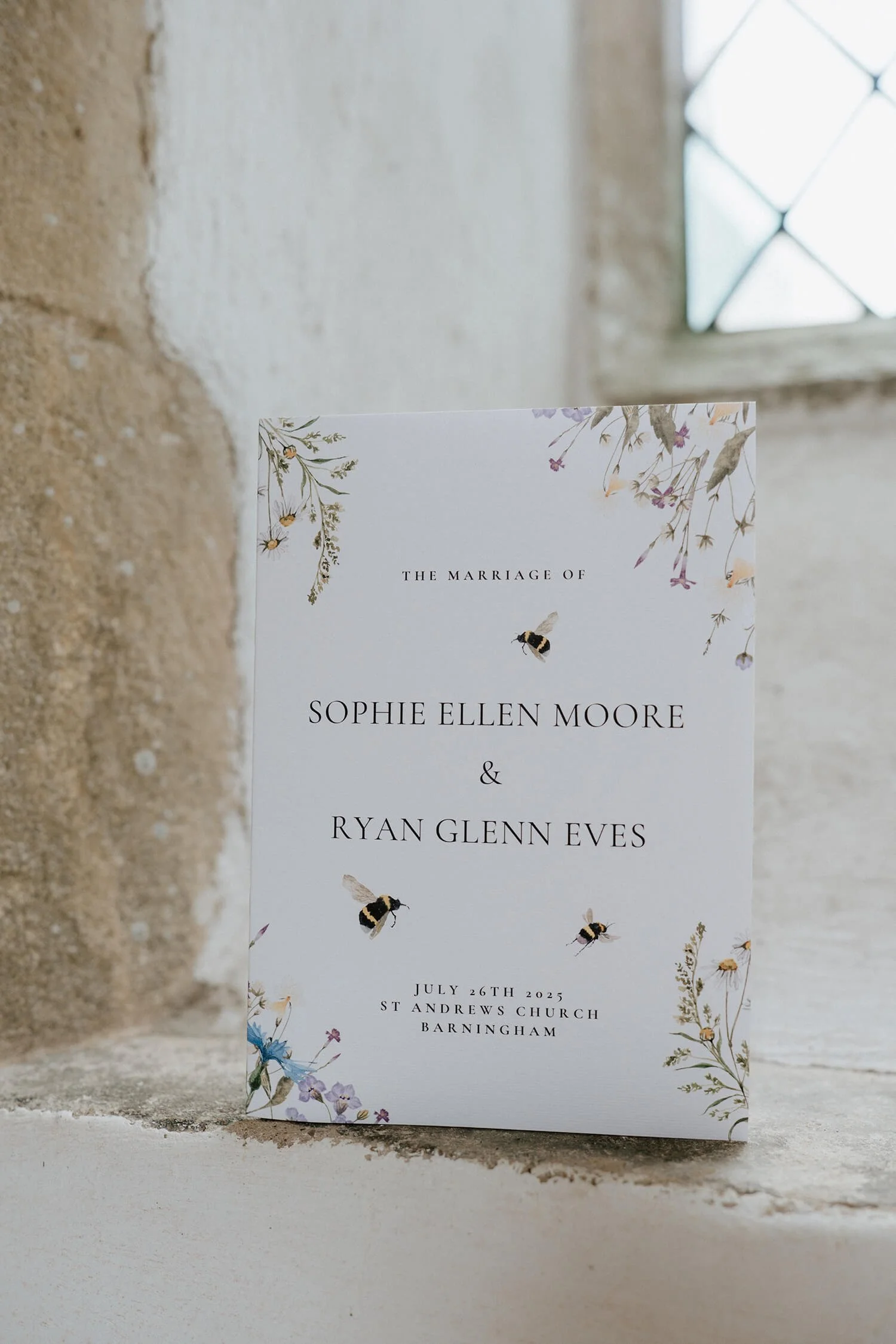 Wedding invitation card with floral and bee illustrations, details of the marriage of Sophie Ellen Moore and Ryan Glenn Eves, July 26th, 2025 at St Andrews Church, Barningham.