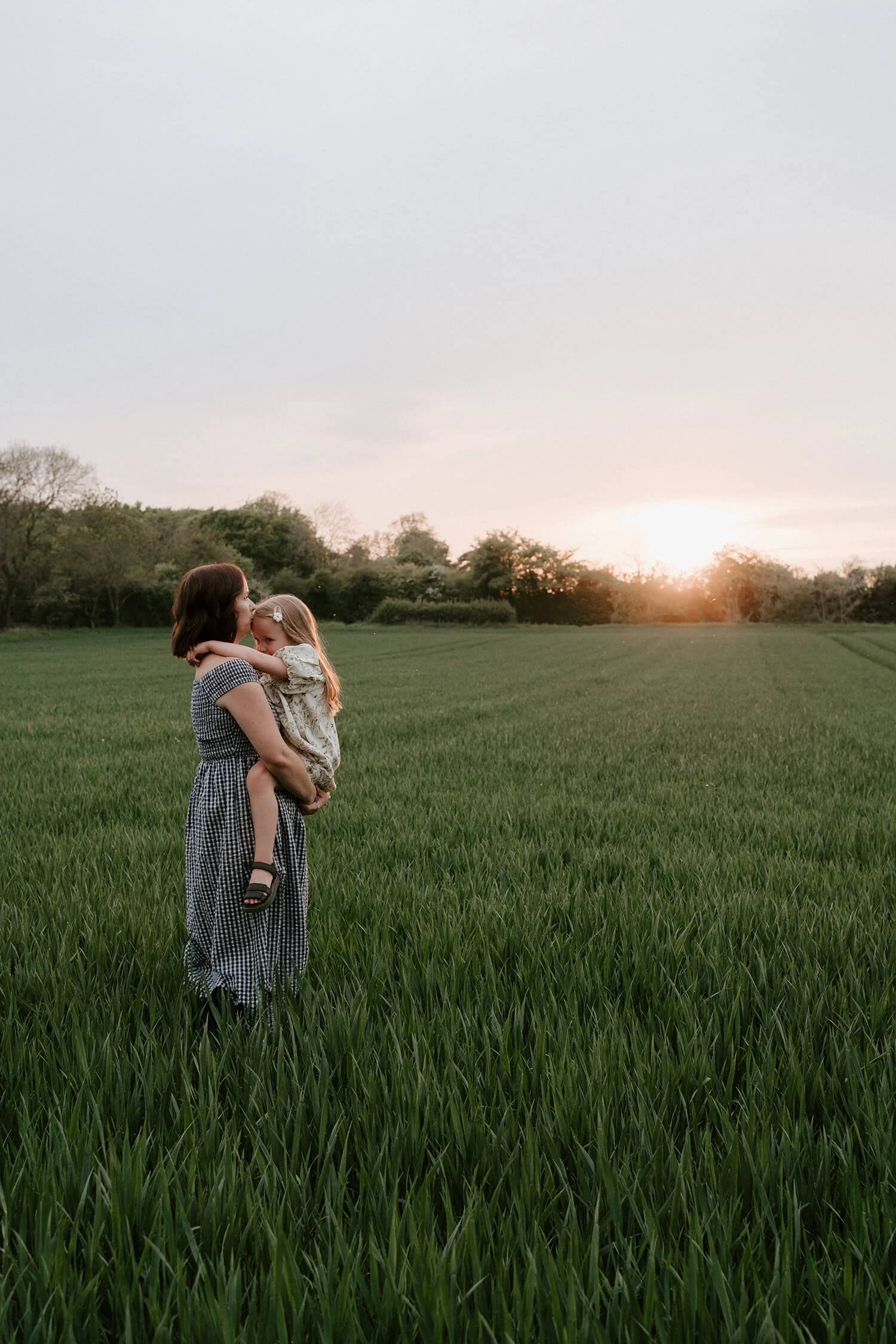 A woman holding a young girl in a grassy field during sunset