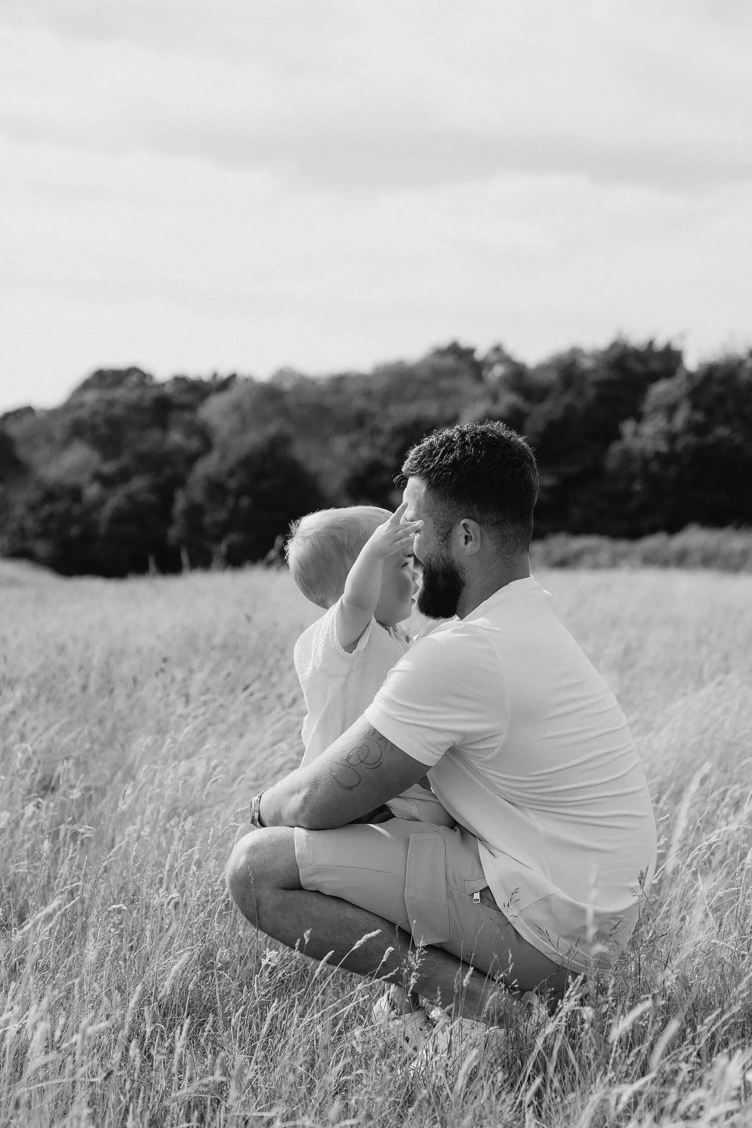 A man and a young child playing in a field, with the child touching the man's face, in black and white.