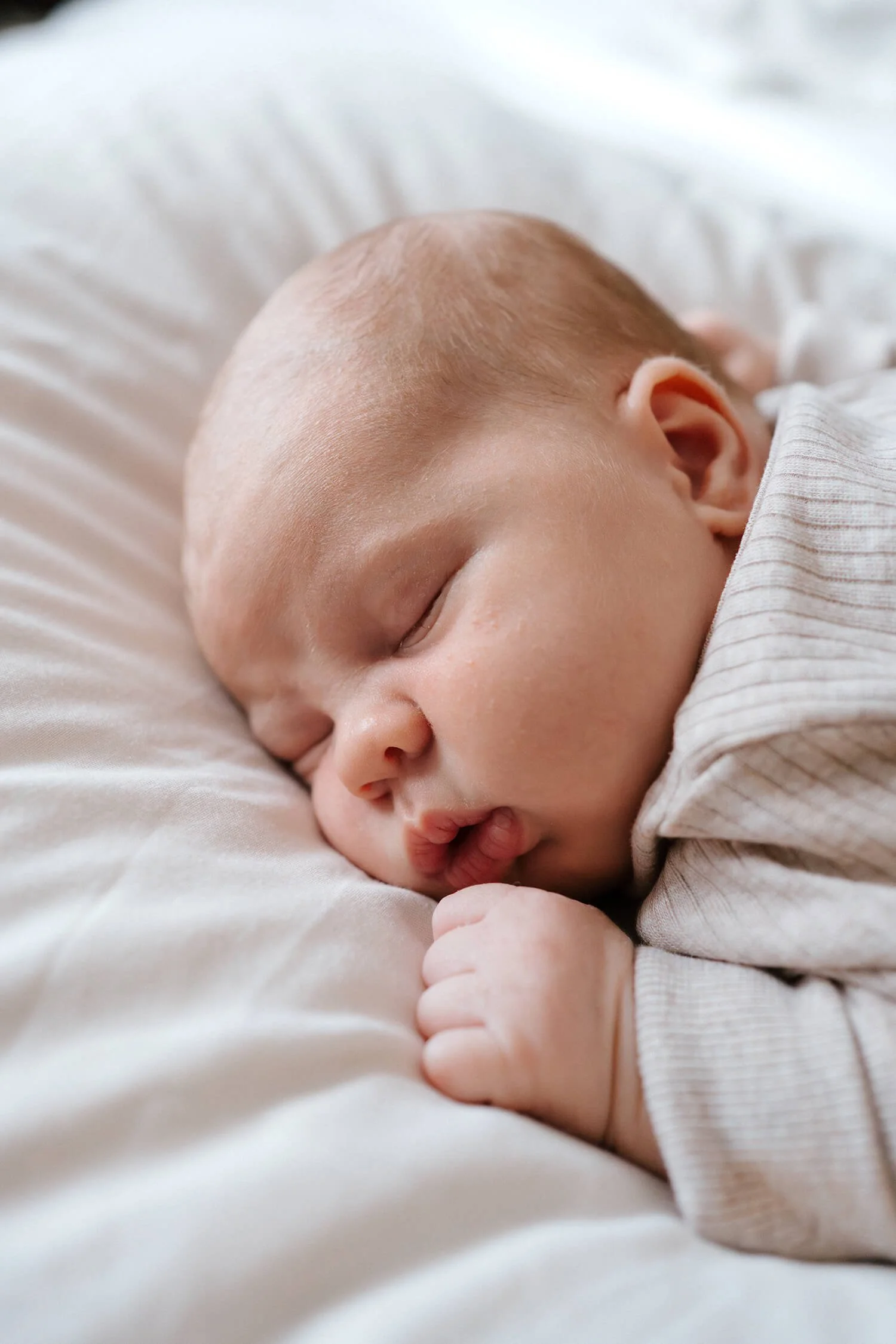 A close-up of a sleeping baby with a peaceful expression, lying on a soft white surface.