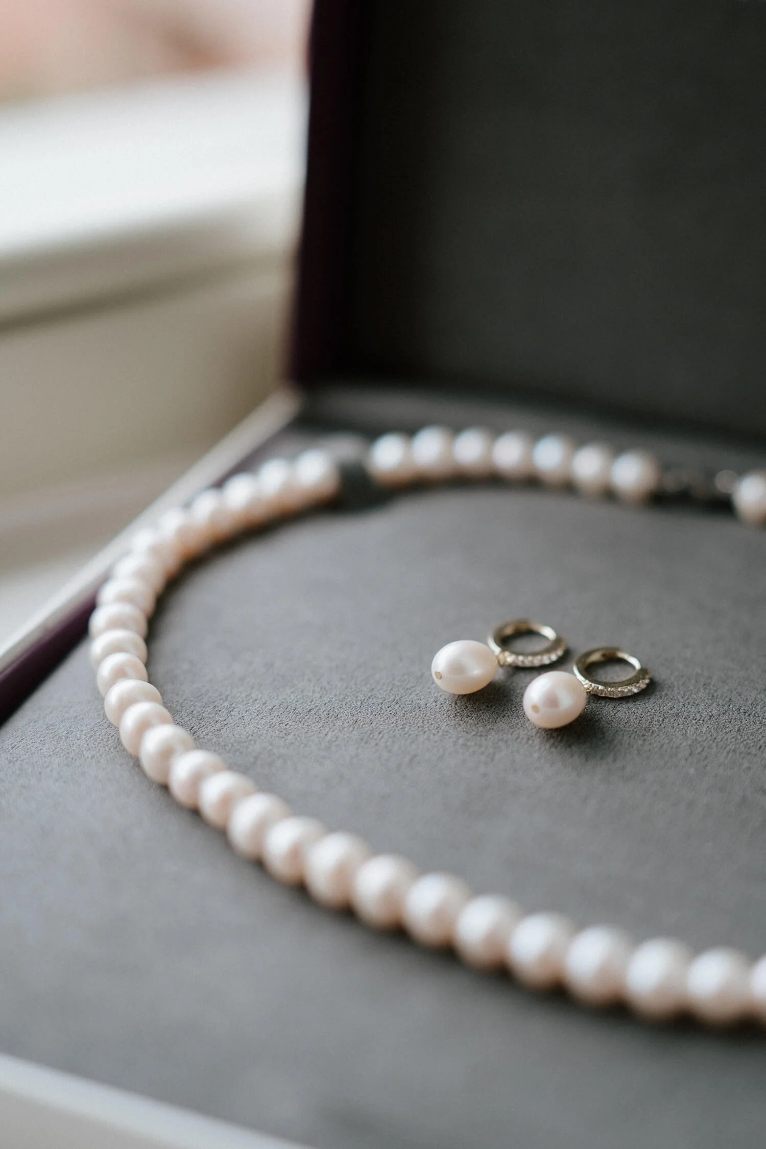 A pearl necklace and a pair of pearl earrings with a small hoop design inside a jewelry box.