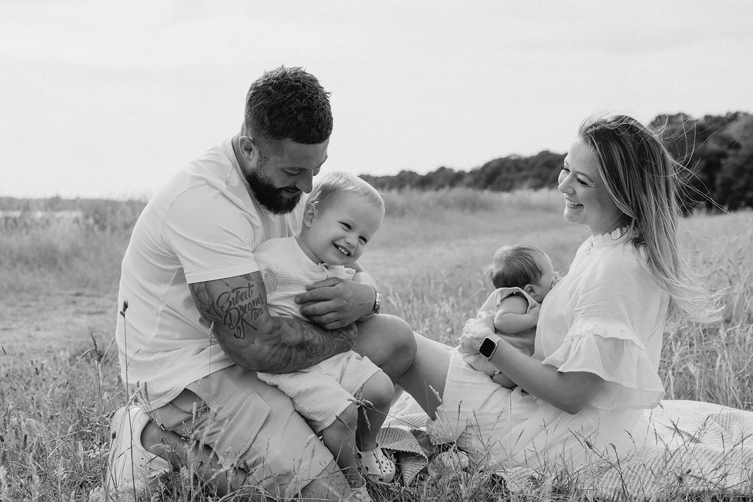 A family of four enjoying a picnic outdoors in a grassy field, with two young children and smiling parents.