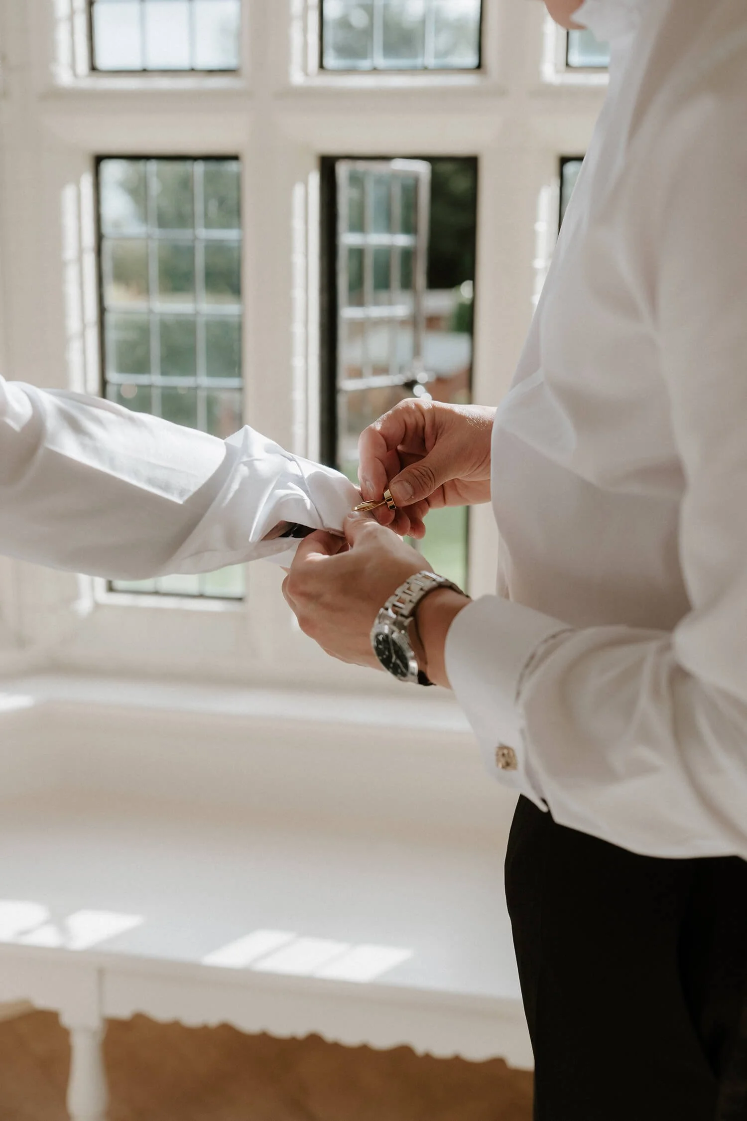 A person adjusting their shirt cuff in front of open windows.