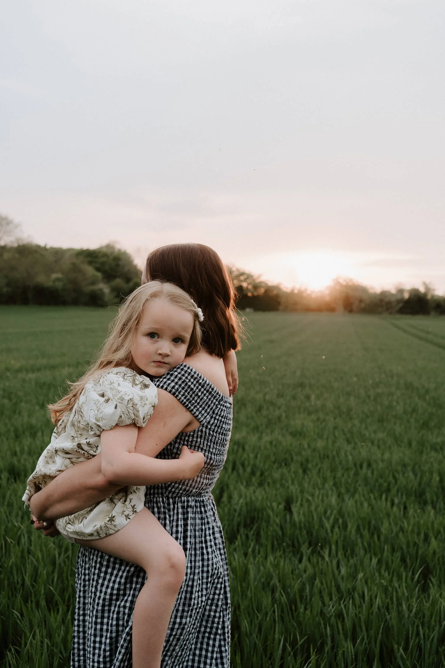 A woman carrying a young girl on her back in a green field during sunset.
