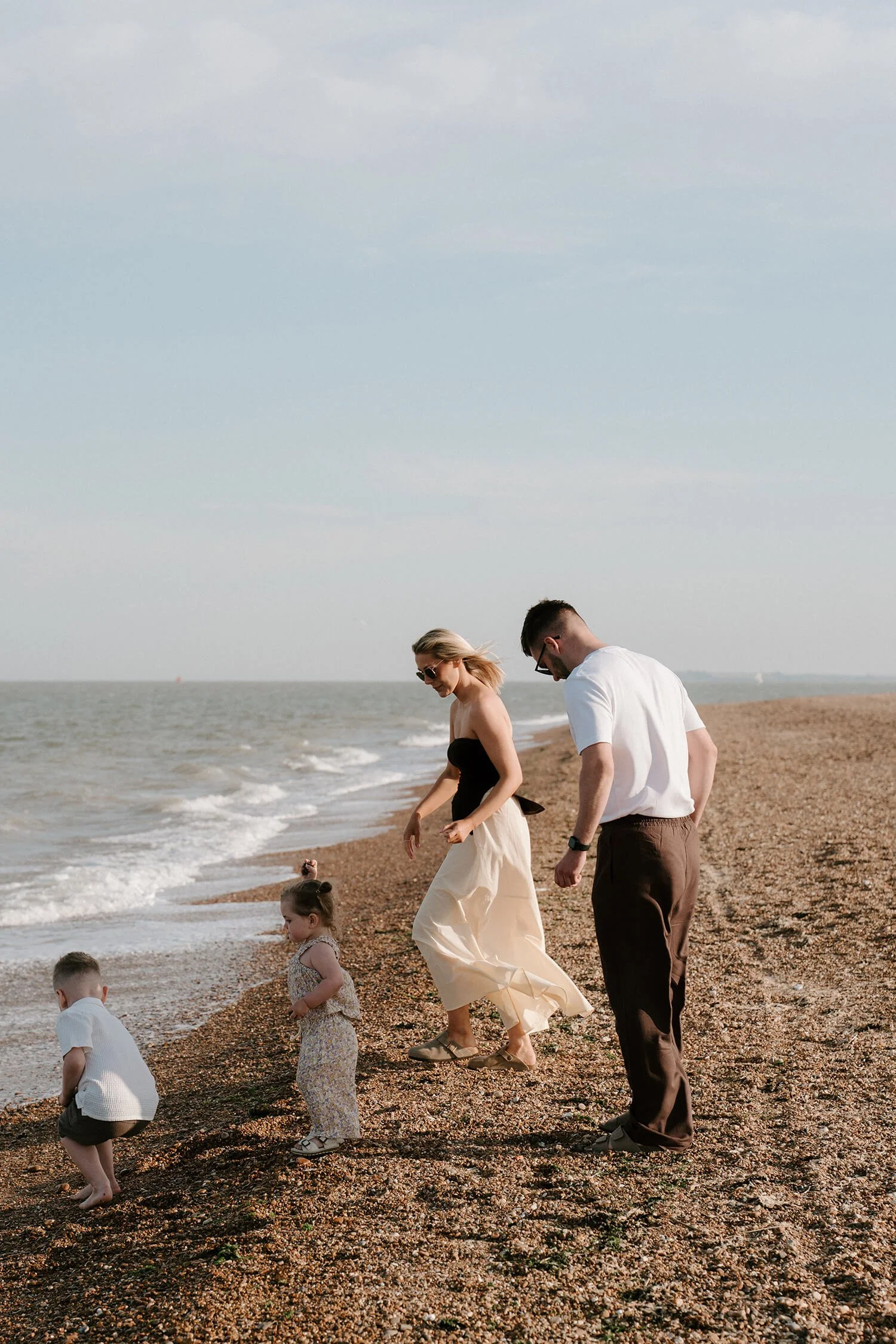 A family of four at the beach, with young children playing near the water and adults watching them.