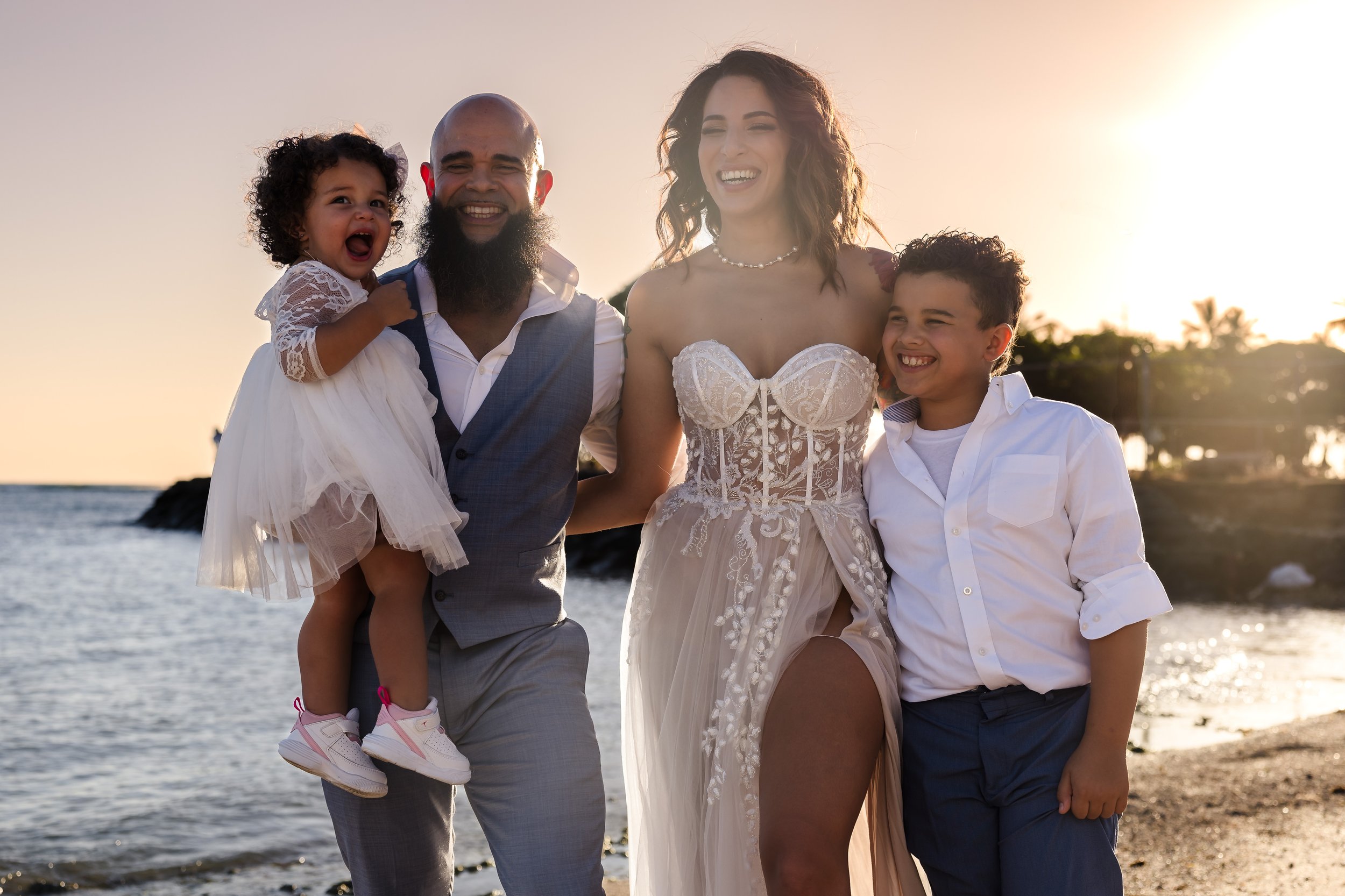 A happy family at the beach during sunset, with a man, woman, and two children smiling and enjoying their time together.