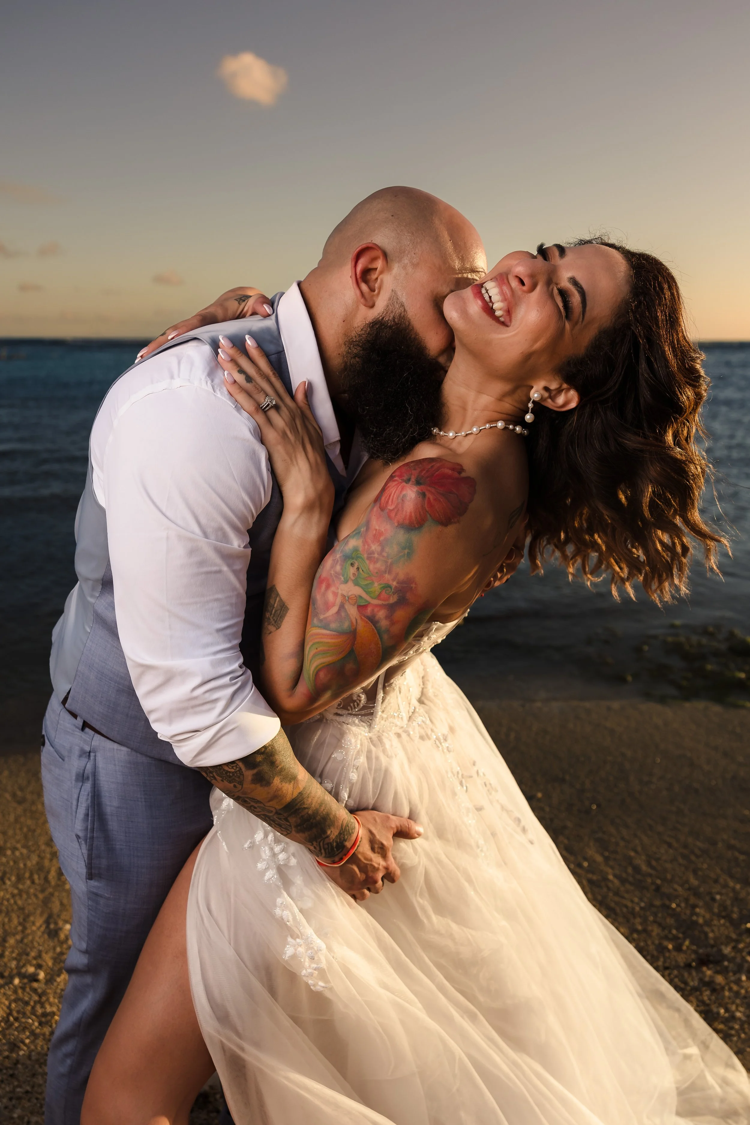 A happy couple at the beach during sunset, sharing a joyful kiss and embracing each other.