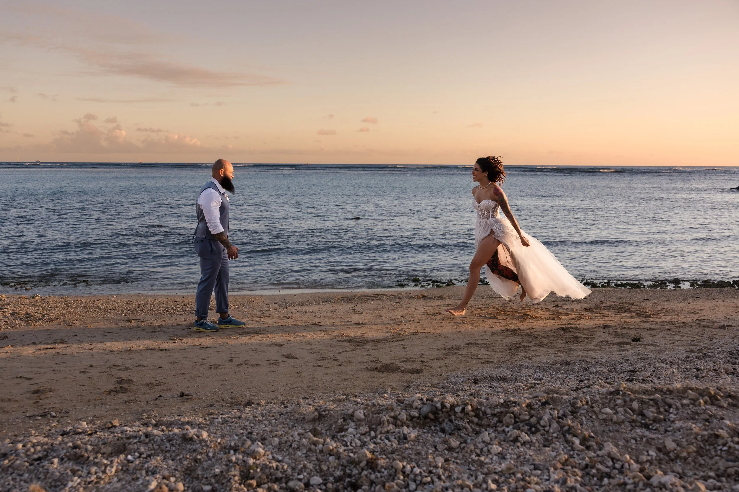 A man and woman on a beach at sunset, with the woman dancing and the man watching.