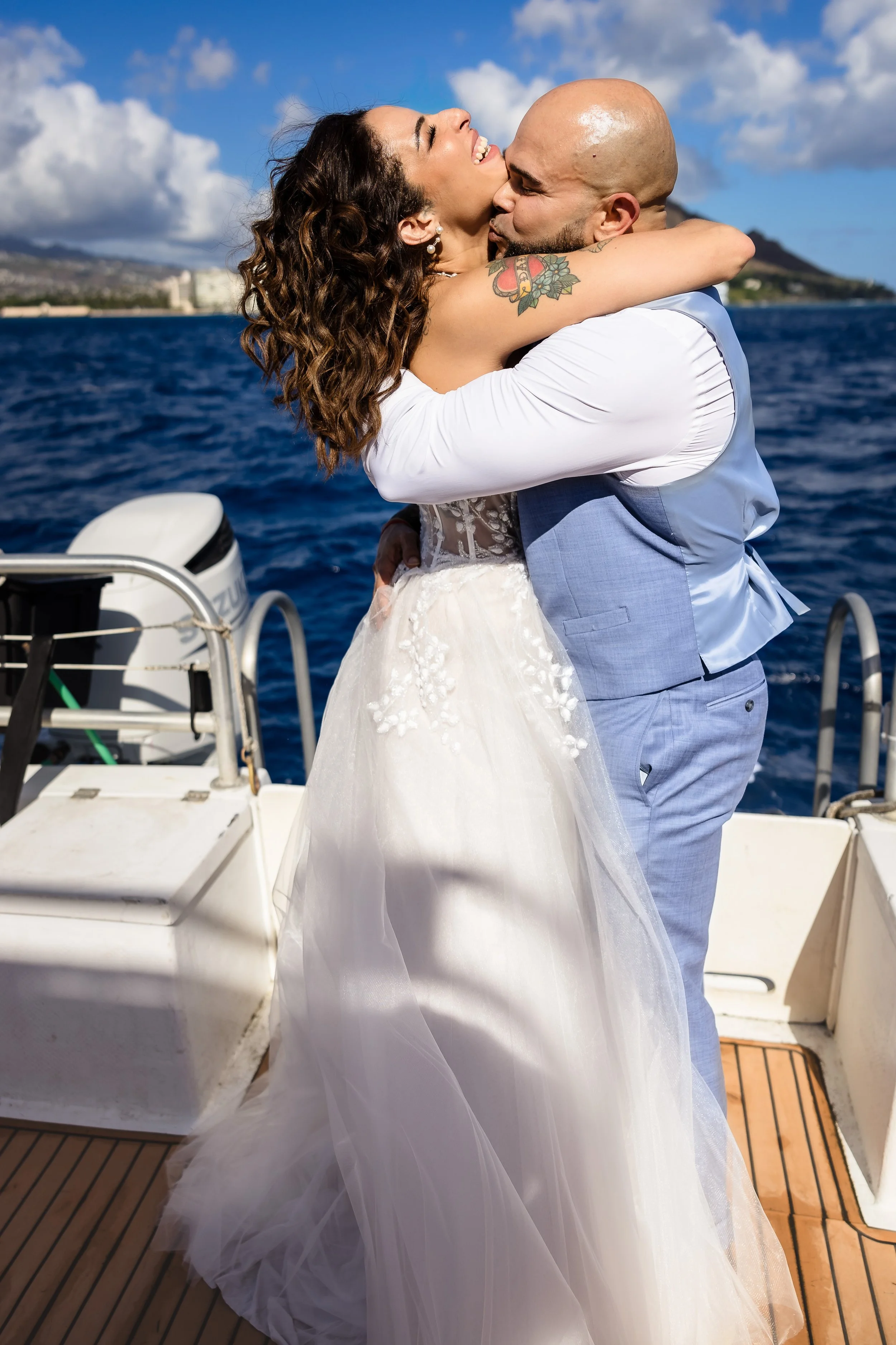 A newlywed couple sharing a joyful embrace on a boat, with the ocean and distant landscape in the background.