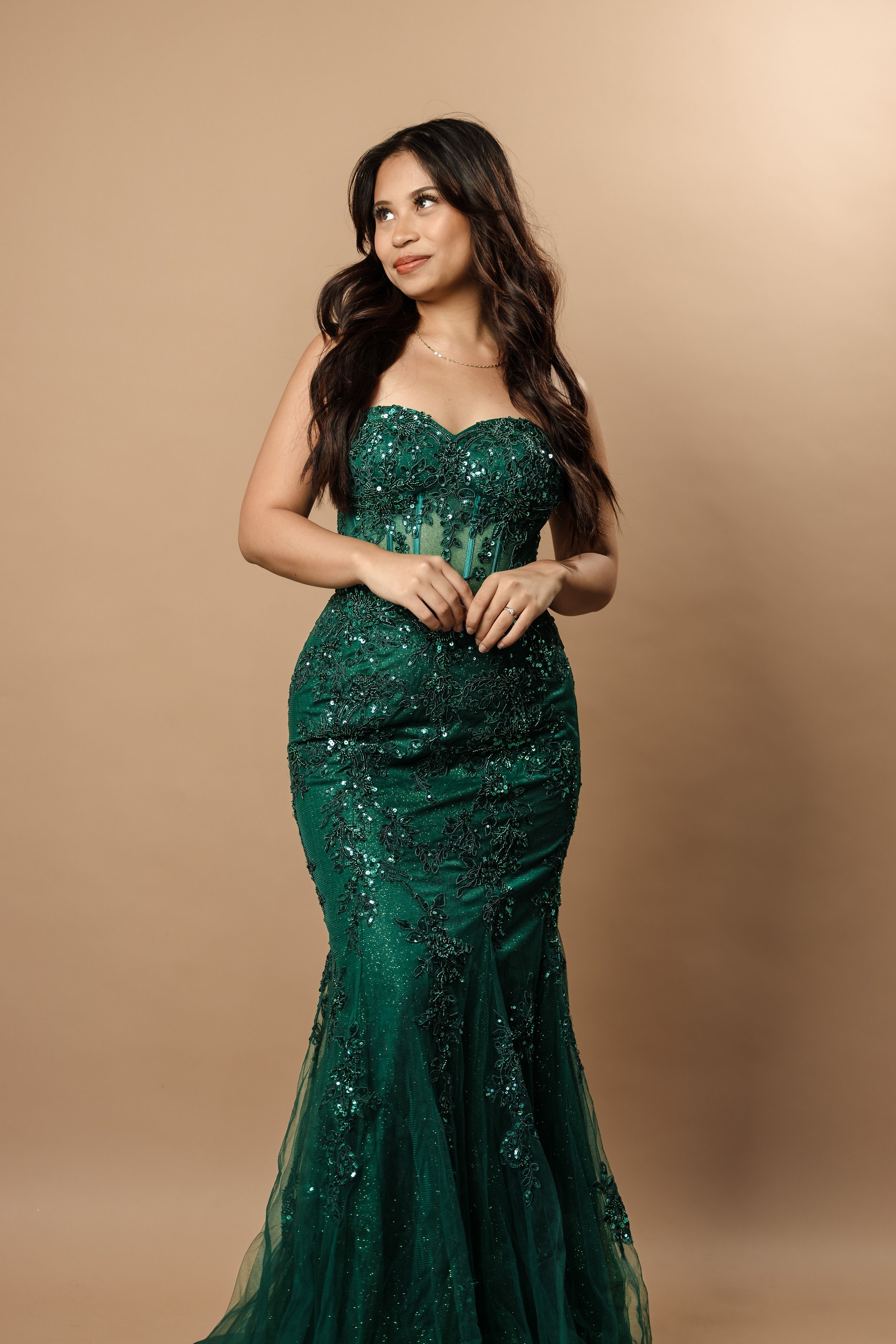 A woman in an elegant green strapless gown with intricate beadwork and embroidery, posing against a neutral background.