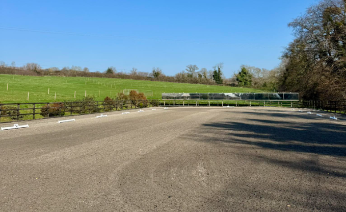 Empty outdoor racing track with green fields and trees in the background under a clear blue sky.