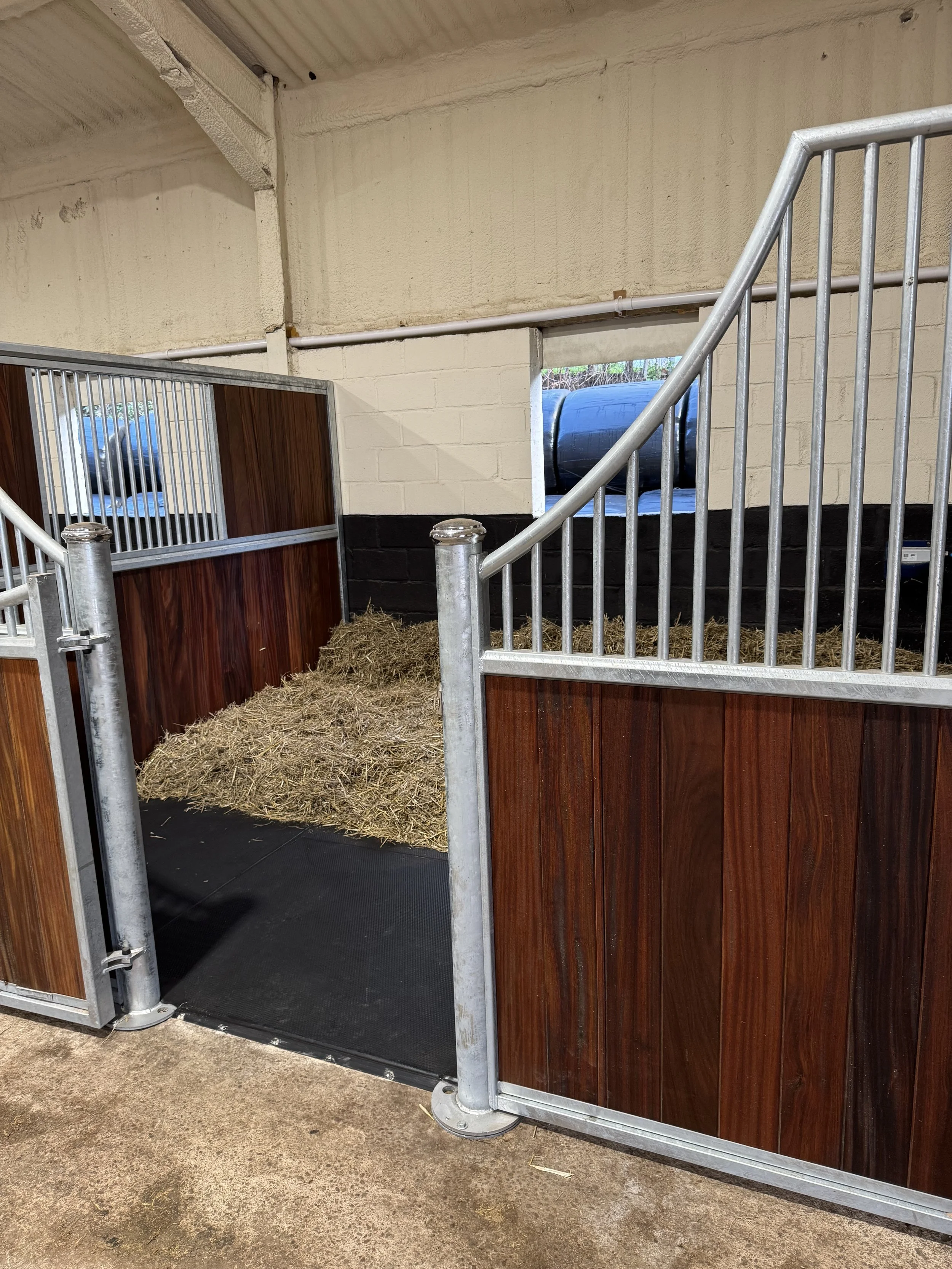 A horse stall with wood and metal fencing, filled with hay, inside a barn or stable.