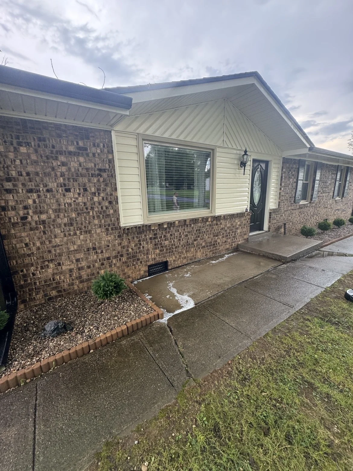 Exterior of a brick and vinyl-sided house with a clean pressure washed concrete sidewalk, windows, and a black front door.