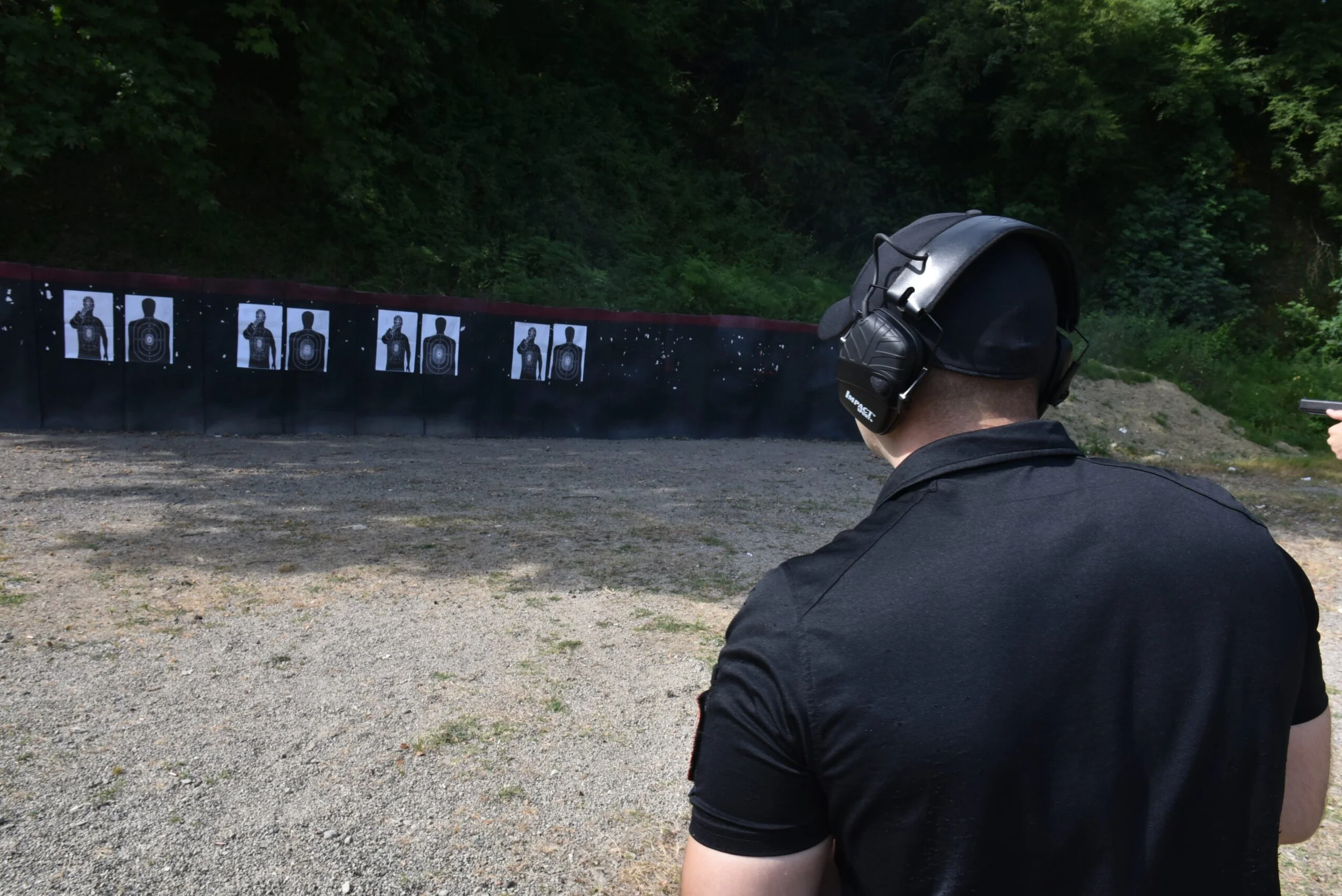 Person at a shooting range aiming at targets with target images of a human silhouette attached to a wall