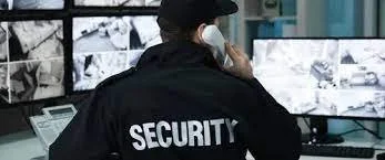 Security officer talking on a phone in front of surveillance monitors.