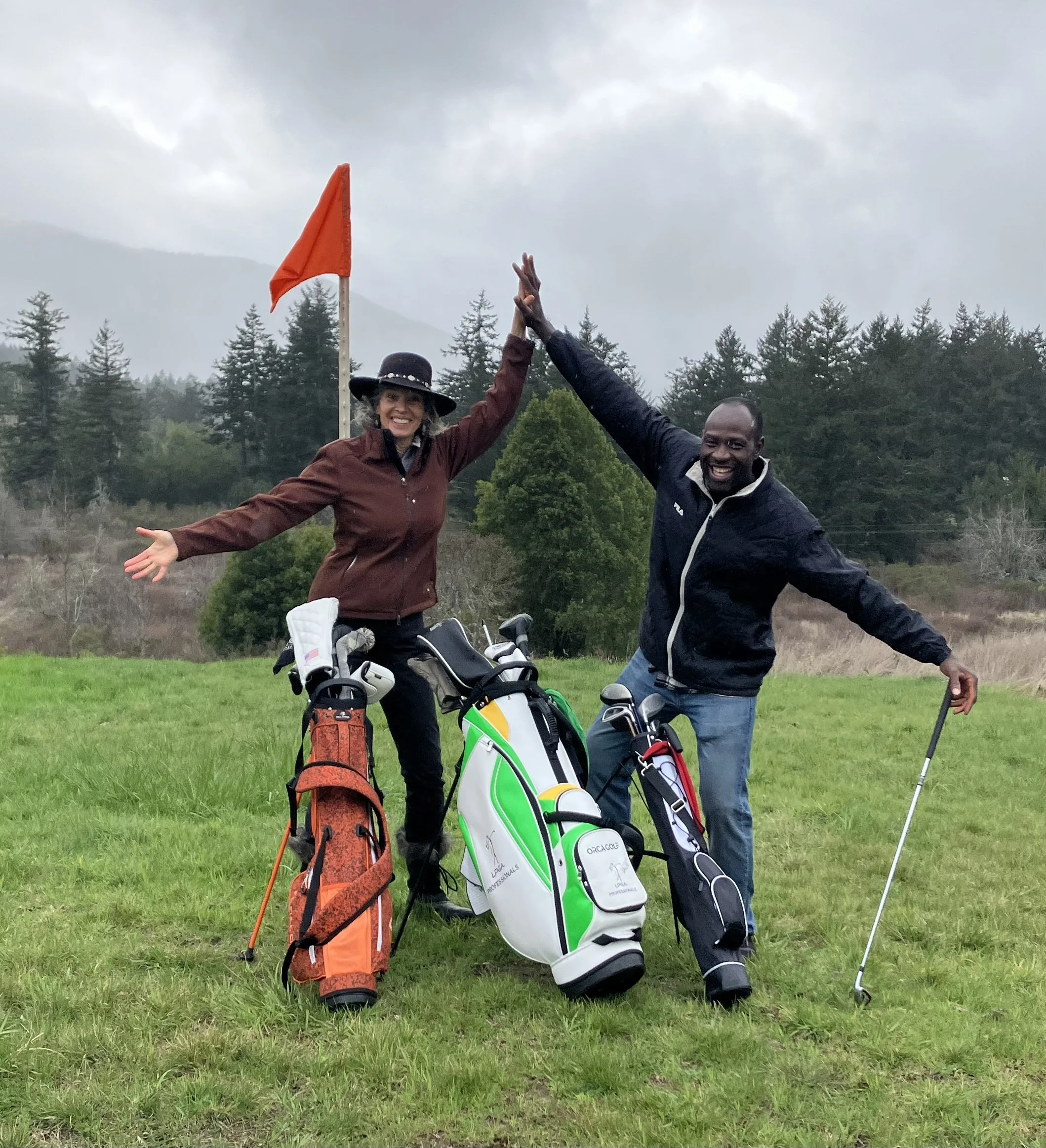 Two golfers celebrating on a golf course with their golf bags and clubs, high-fiving each other, in a cloudy outdoor setting with trees in the background.